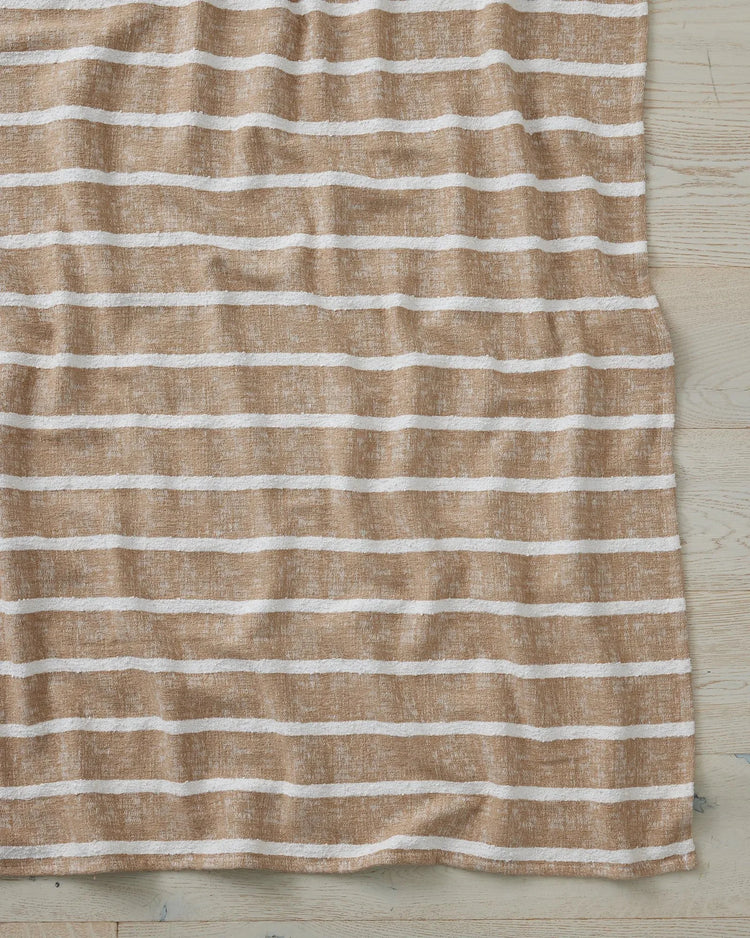 Neutral striped throw in beige and cream with soft linen texture, draped on light wooden flooring in a serene coastal-inspired interior setting