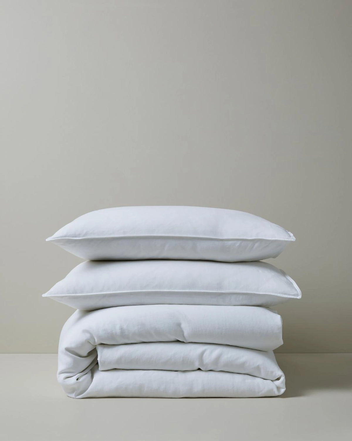Stacked white linen bedding in minimalist aesthetic, featuring Ravello quilt cover and pillowcases with soft natural texture against neutral backdrop