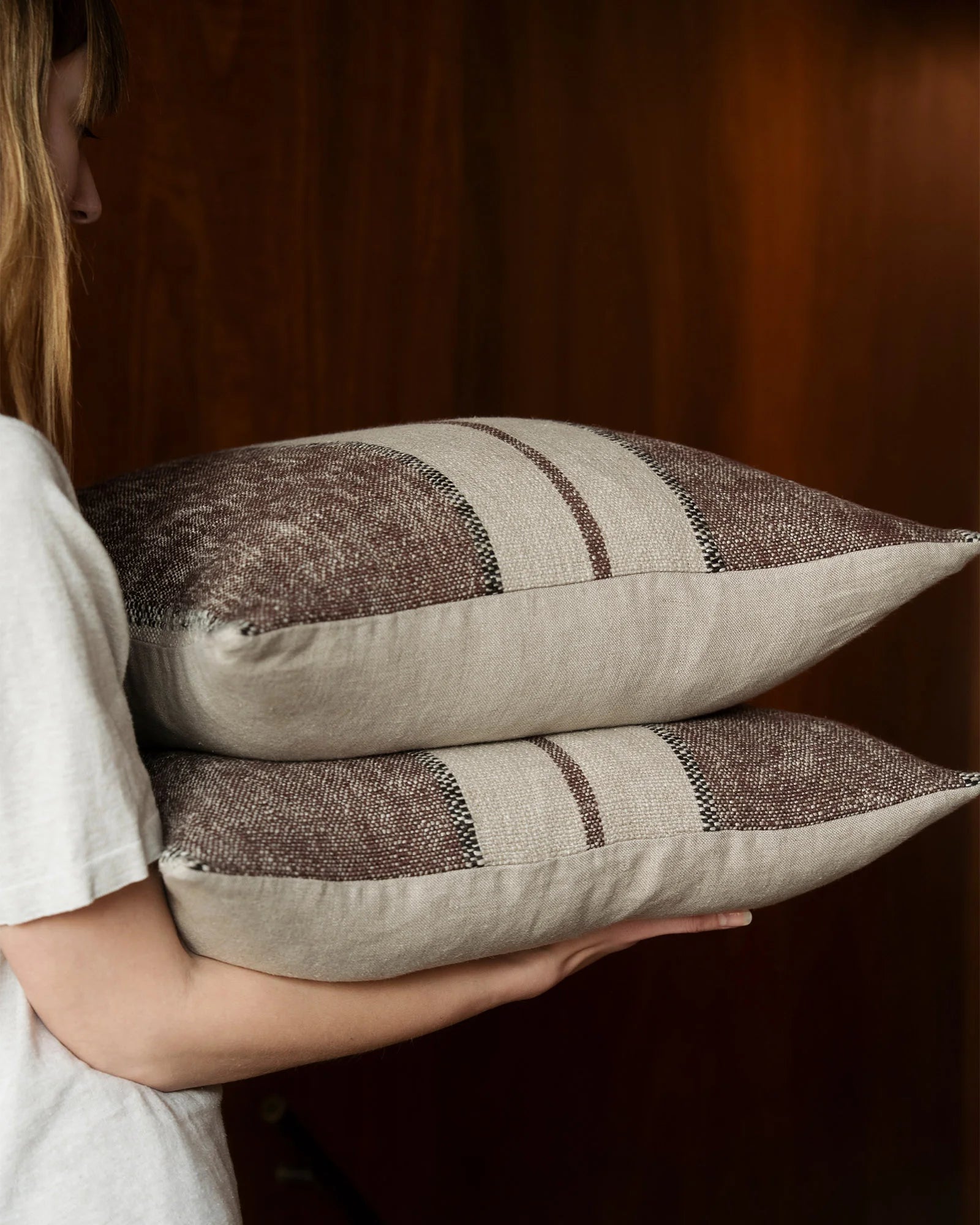 Neutral striped linen-blend cushions with warm brown tones, styled against rich chocolate backdrop for earthy, minimalist home décor aesthetic