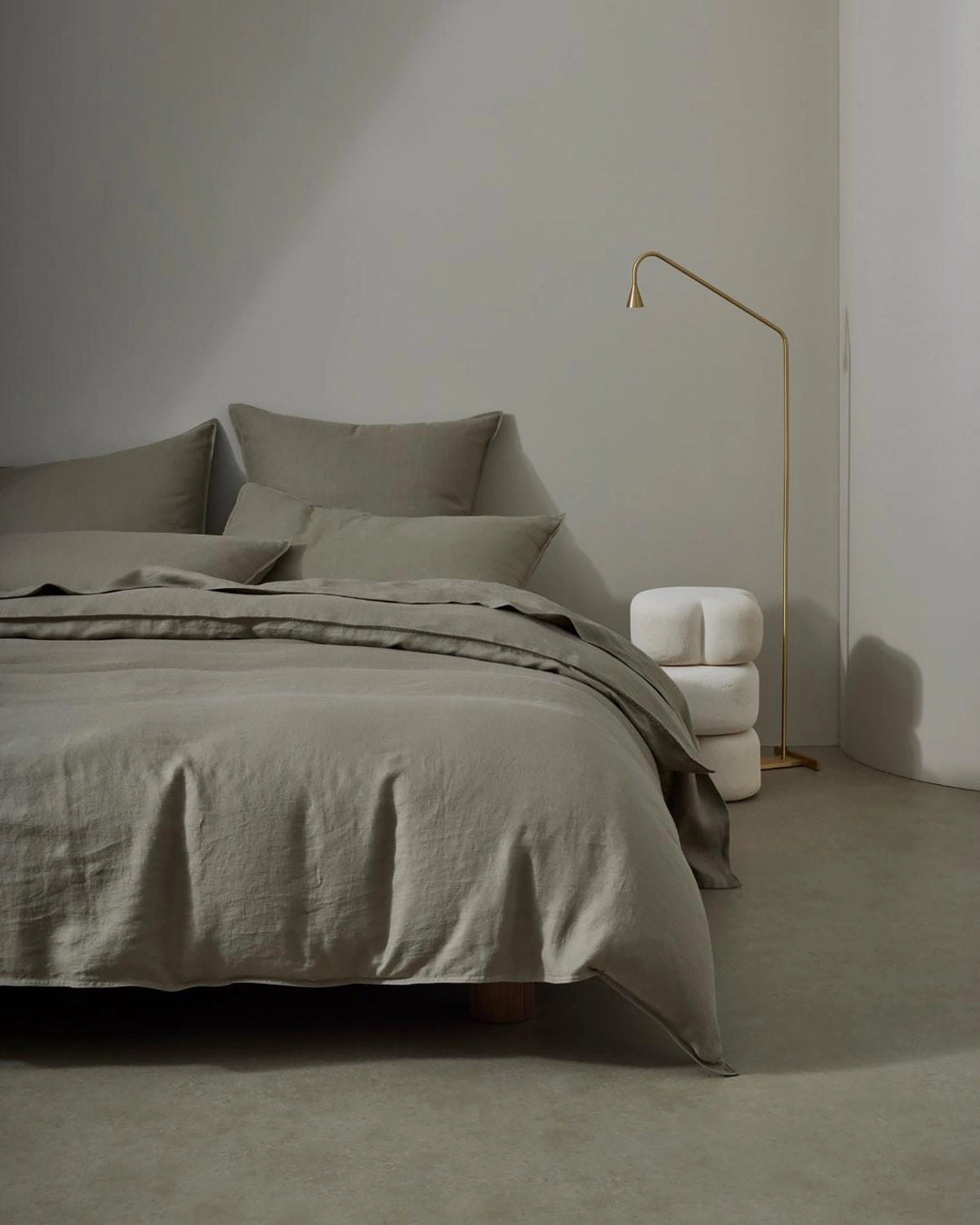 Minimalist bedroom with sage linen bedding and pillows, brass floor lamp, neutral palette, soft natural textures and understated monochrome styling
