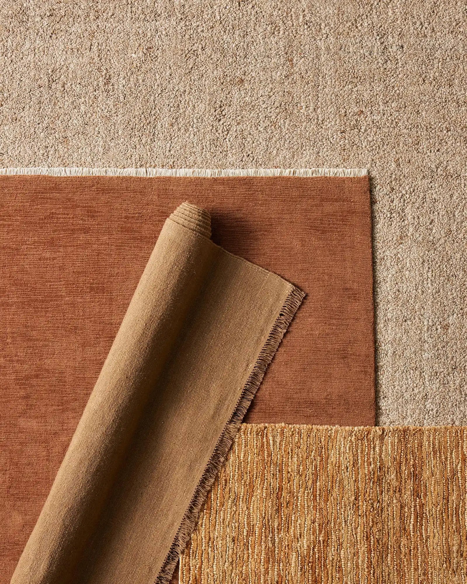 Layered rugs in warm earth tones: terracotta linen and natural jute textures create depth, showcasing neutral palette and woven material details