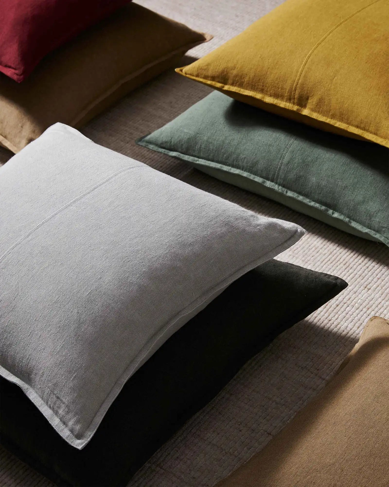 Linen cushions in muted earth tones—grey, sage, charcoal, ochre—arranged on neutral fabric, showcasing natural texture and minimalist interior styling