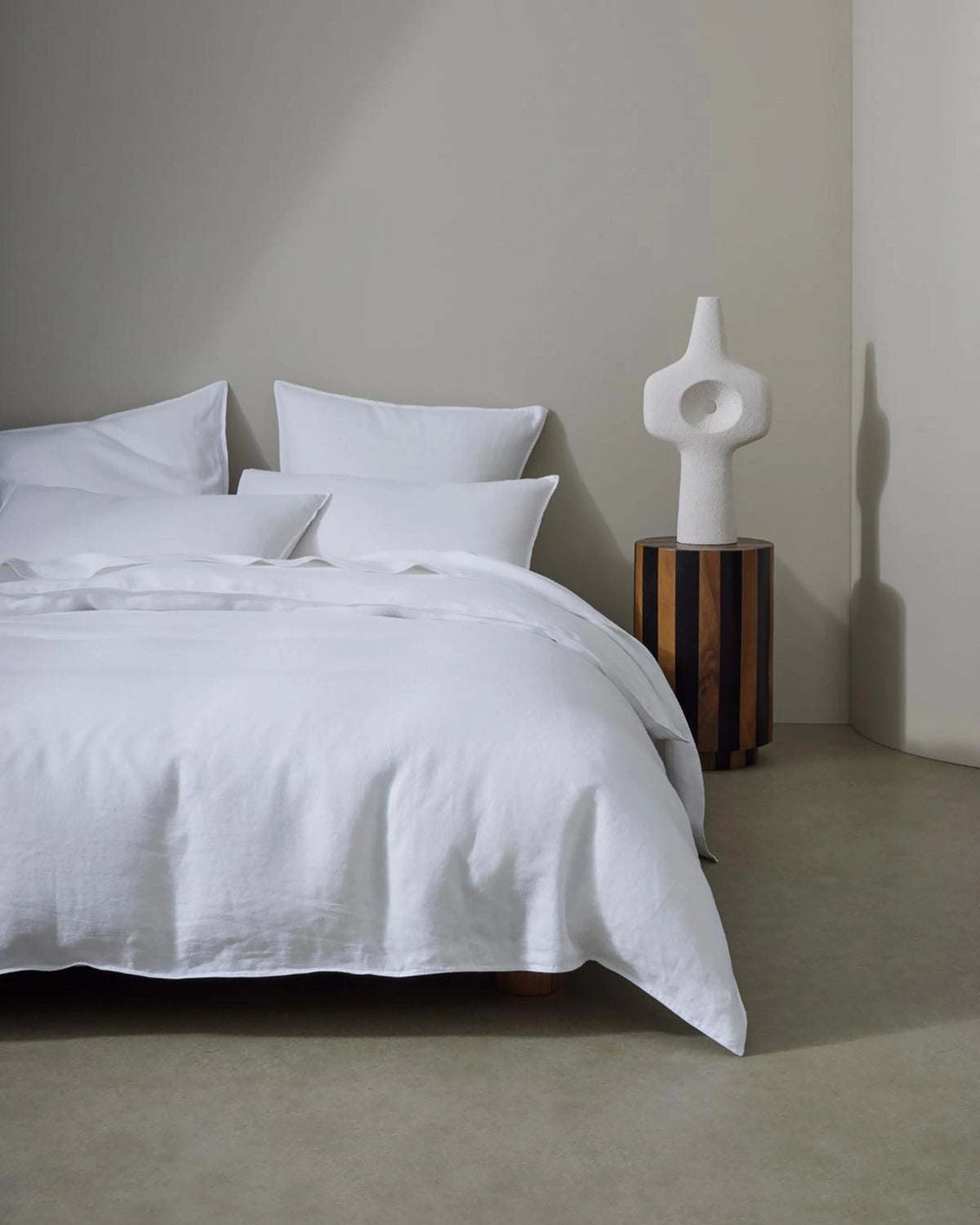 Minimalist bedroom styled with crisp white European linen bedding from the Ravello range, paired with warm wood tones and sculptural decor in a neutral colour palette