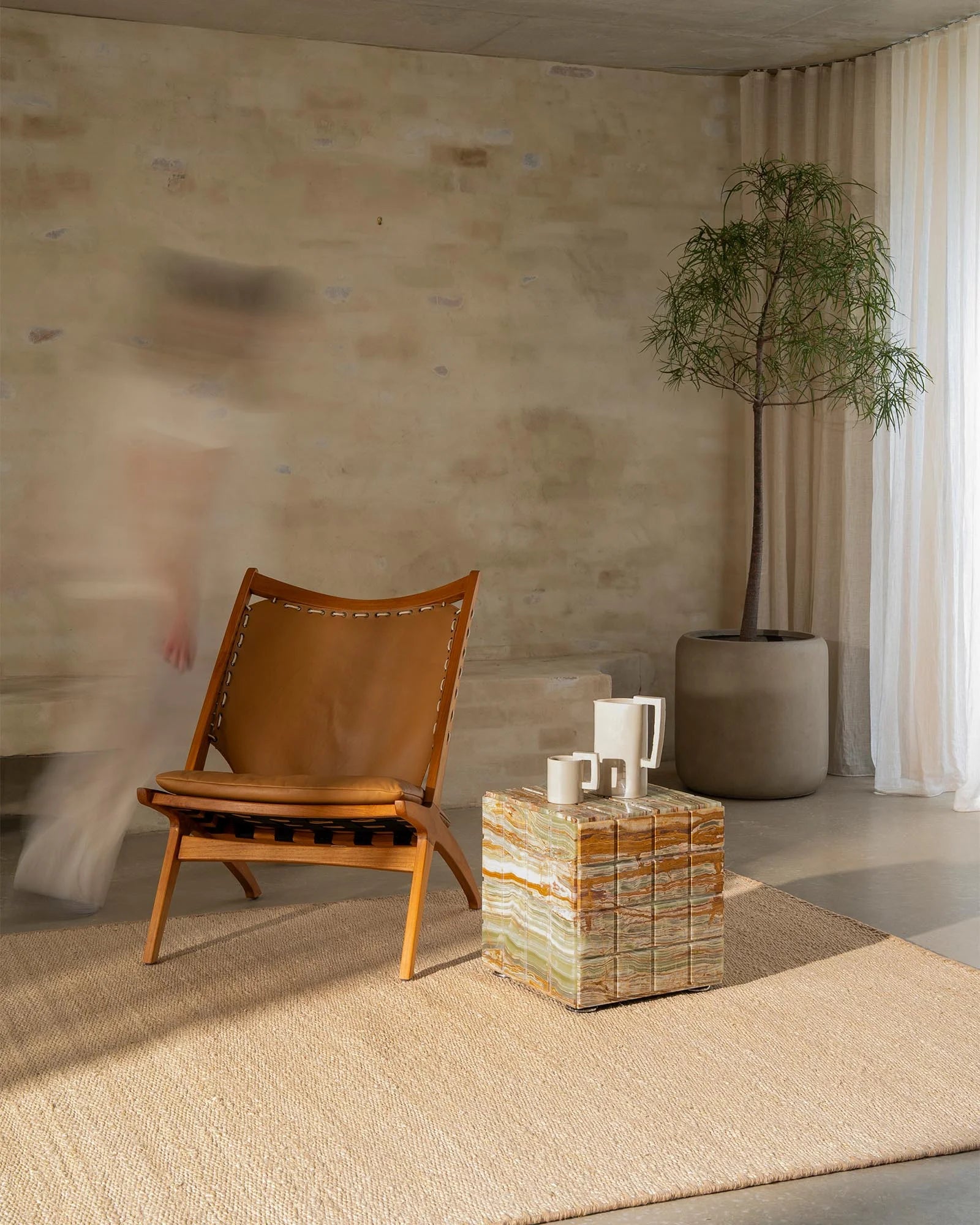 Neutral minimalist living room with oat-toned Monroe rug, cognac leather lounge chair, and soft cream curtains creating warm earthy aesthetic