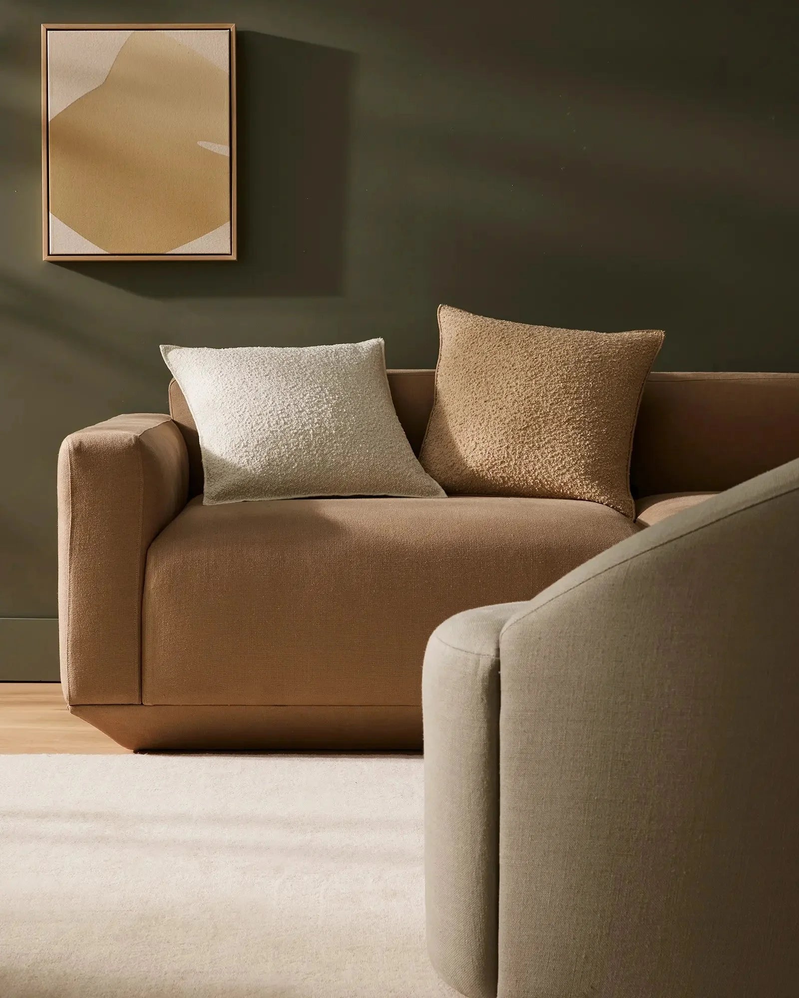 Warm neutral living room with caramel and cream sectional, styled with Alberto ivory and nougat cushions in textured fabrics, olive walls, and abstract wall art