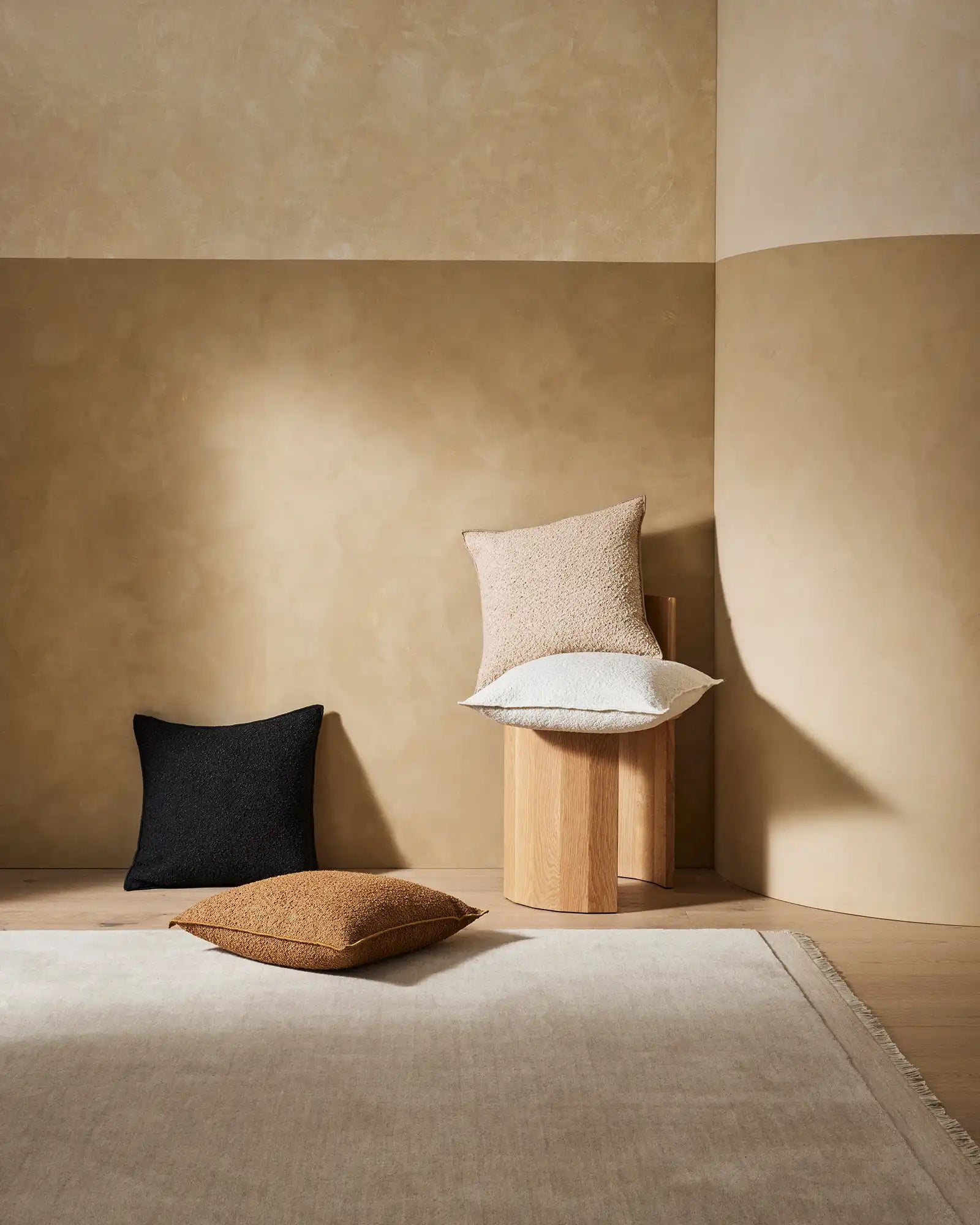 Minimalist living room with warm neutral palette featuring Alberto cushions in copper, ivory, onyx and nougat tones arranged on natural wood and linen, bathed in soft sunlight