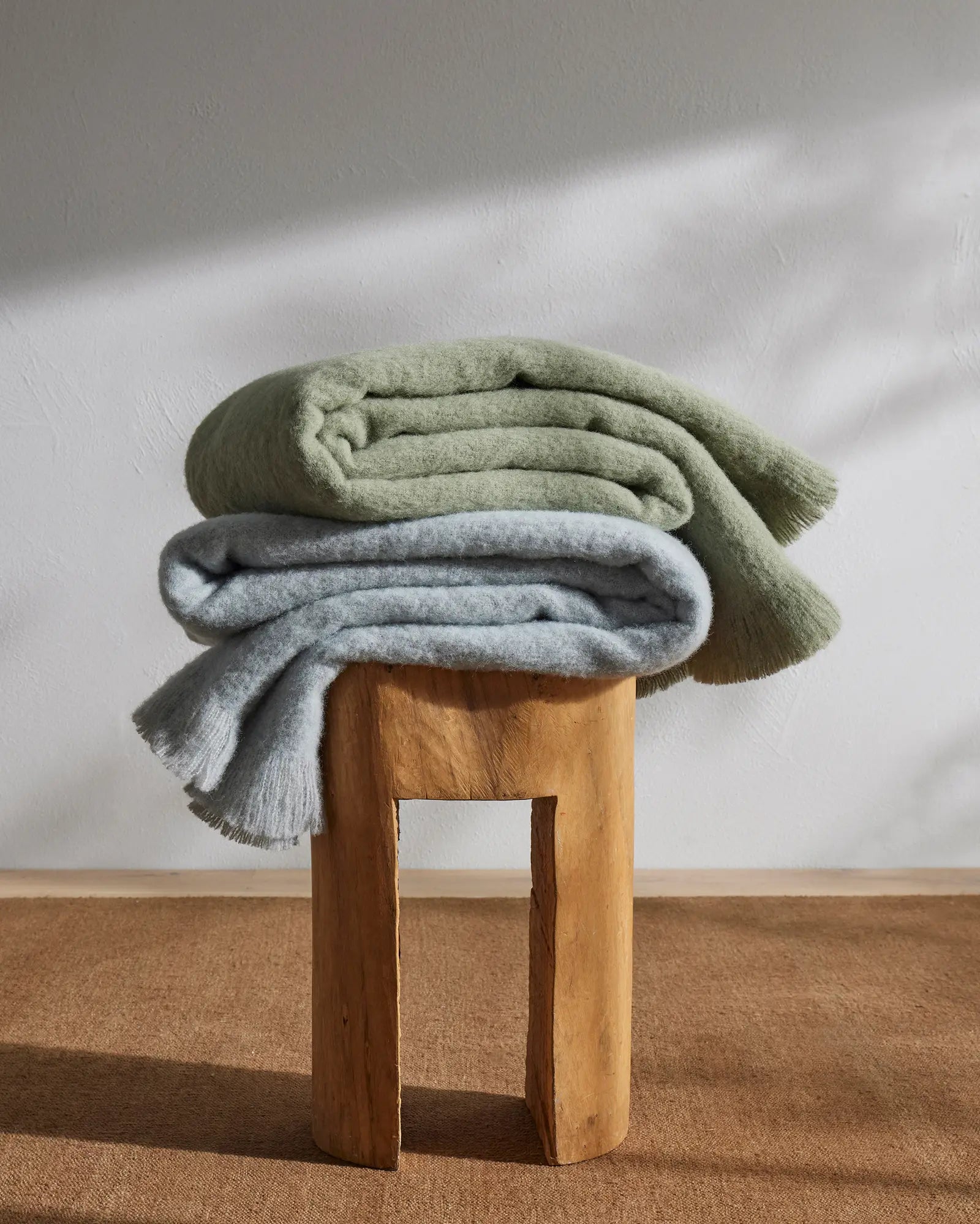 Hyde Breeze woven wool blend throw in sage green and grey, stacked with fringe edges, by Weave Home