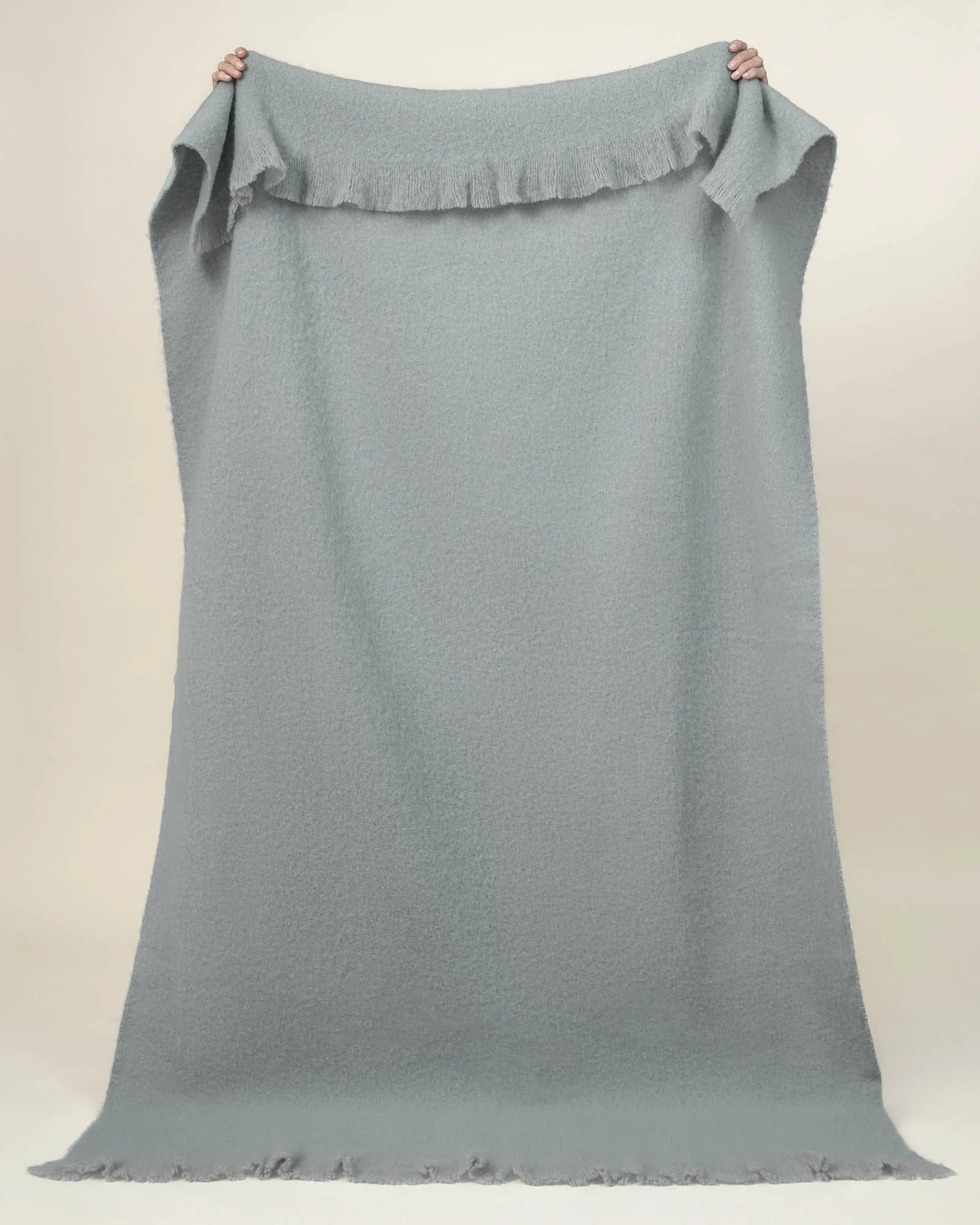 Hyde Breeze wool blend throw in soft blue, woven with brushed finish and fringed border, held up on neutral background by Weave Home