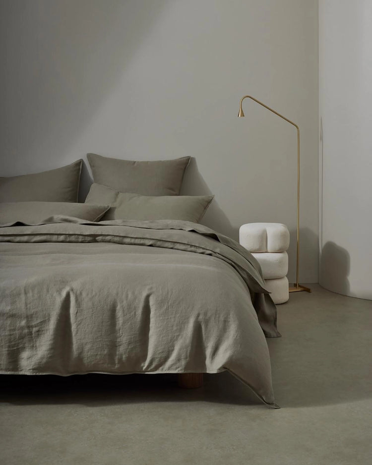 Minimalist bedroom with sage linen bedding and pillows, brass floor lamp, neutral palette, soft natural textures and understated monochrome styling