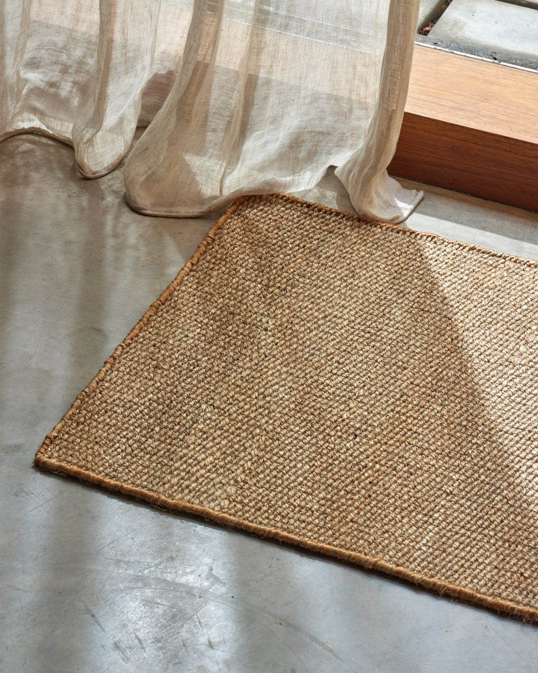 Neutral linen curtains pool beside a woven jute doormat in a light-filled entryway, mixing soft fabric textures with natural fiber flooring.