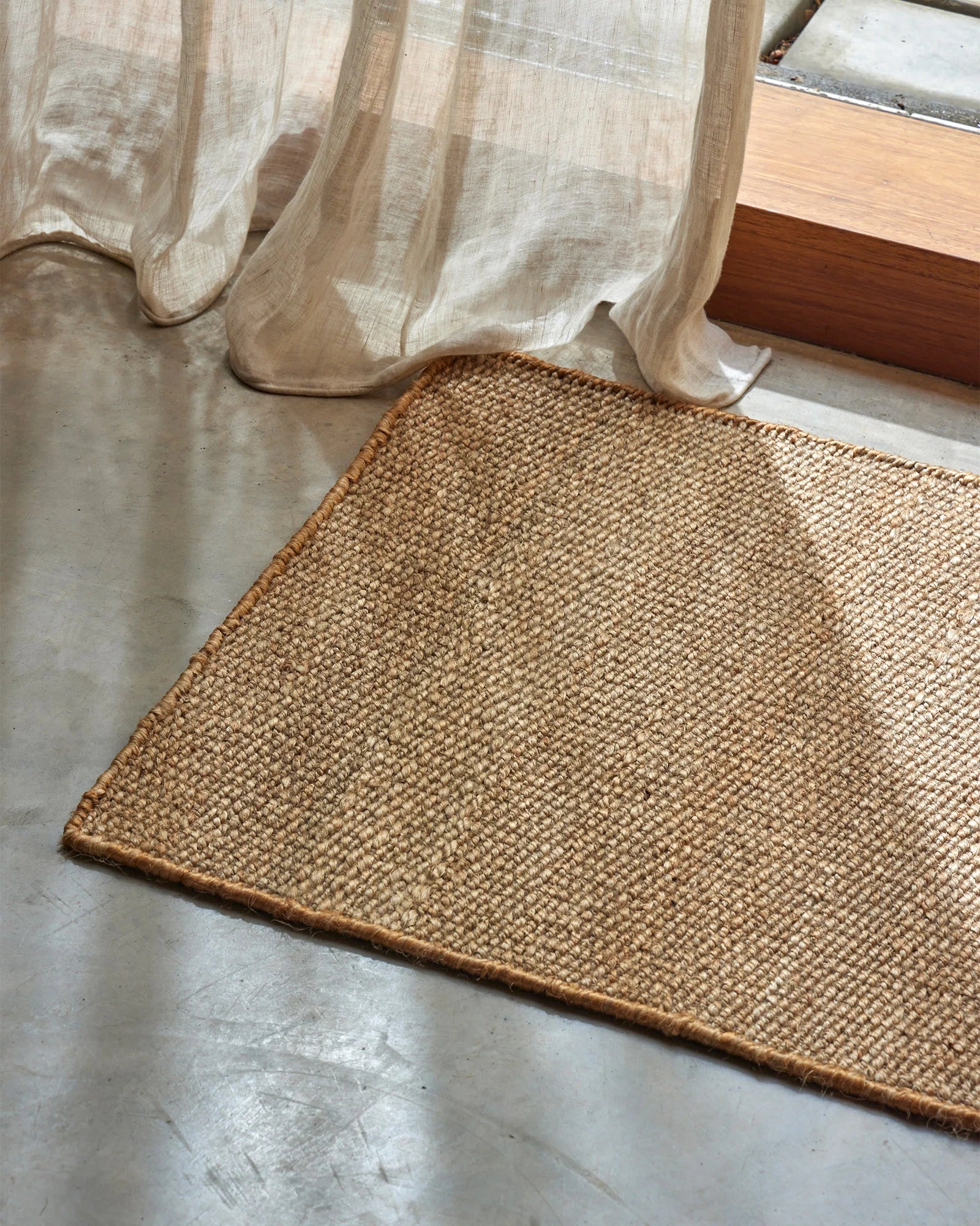 Neutral linen curtains pool beside a woven jute doormat in a light-filled entryway, mixing soft fabric textures with natural fiber flooring.