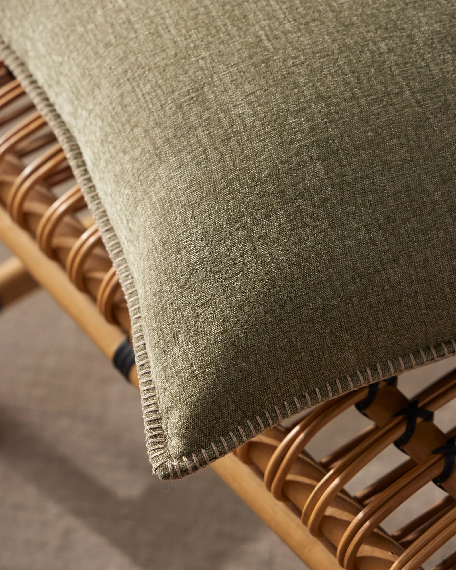 Sage green linen cushion with blanket stitch edge detail draped over timber chair with woven rattan details, natural textile styling
