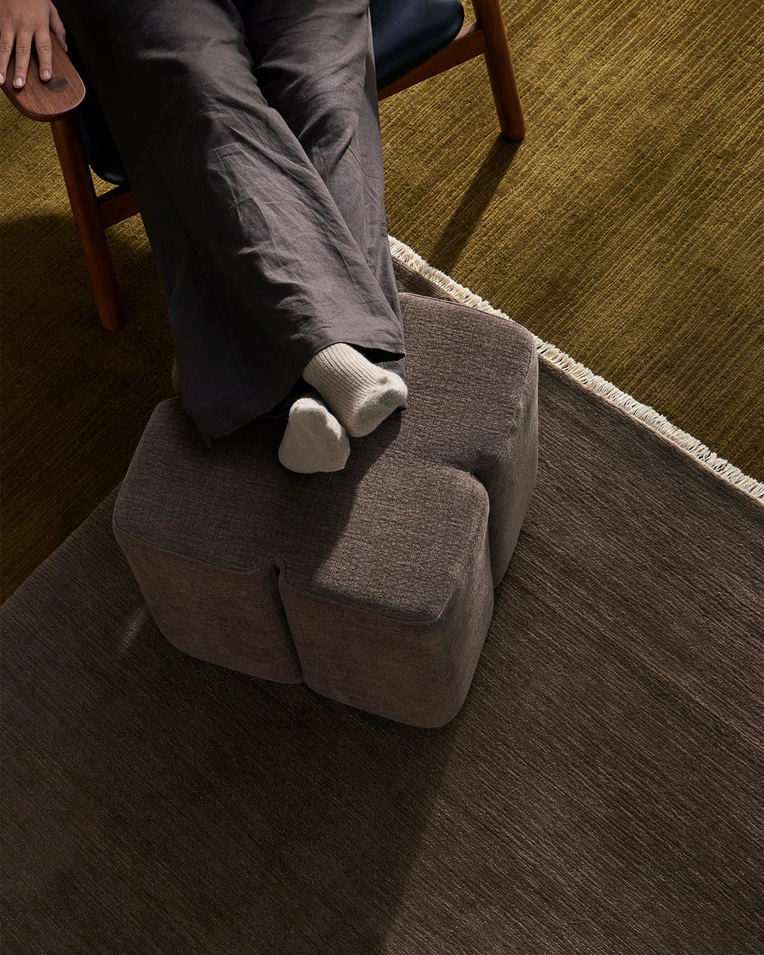 Neutral living room scene with a taupe linen ottoman in earthy mustard and charcoal palette, styled with cream socks and charcoal trousers for cosy home comfort