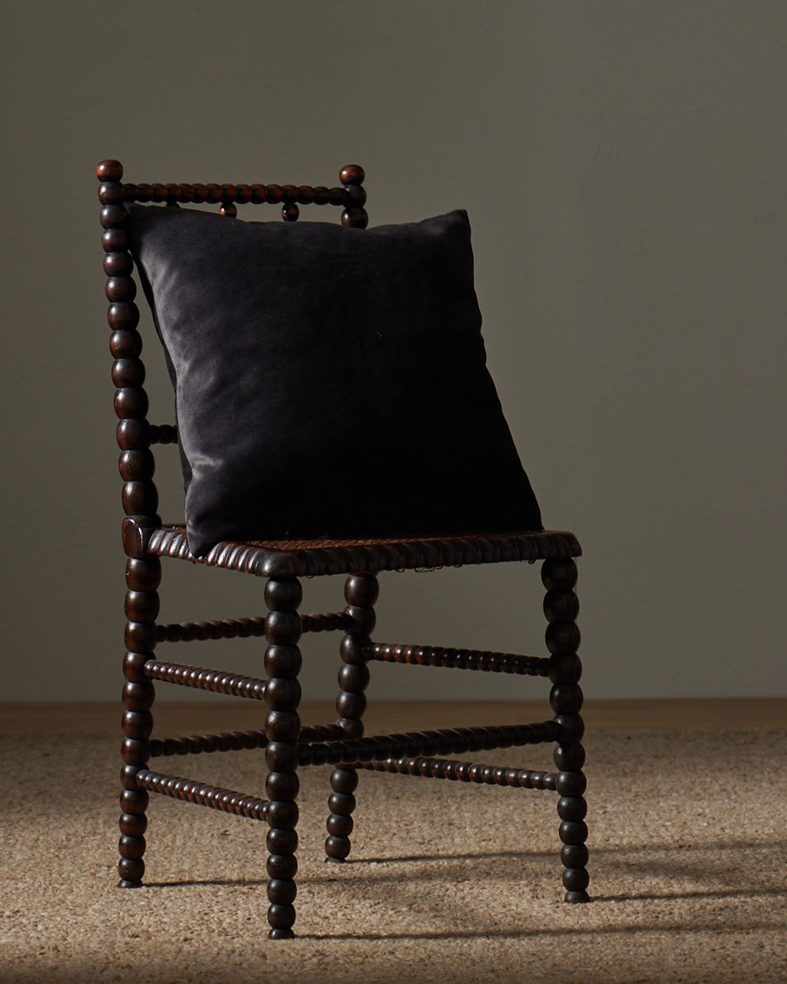 Ava Coal cushion in charcoal, 50x50cm, displayed on wooden spindle chair showing soft velvet-like polyester texture by Weave Home