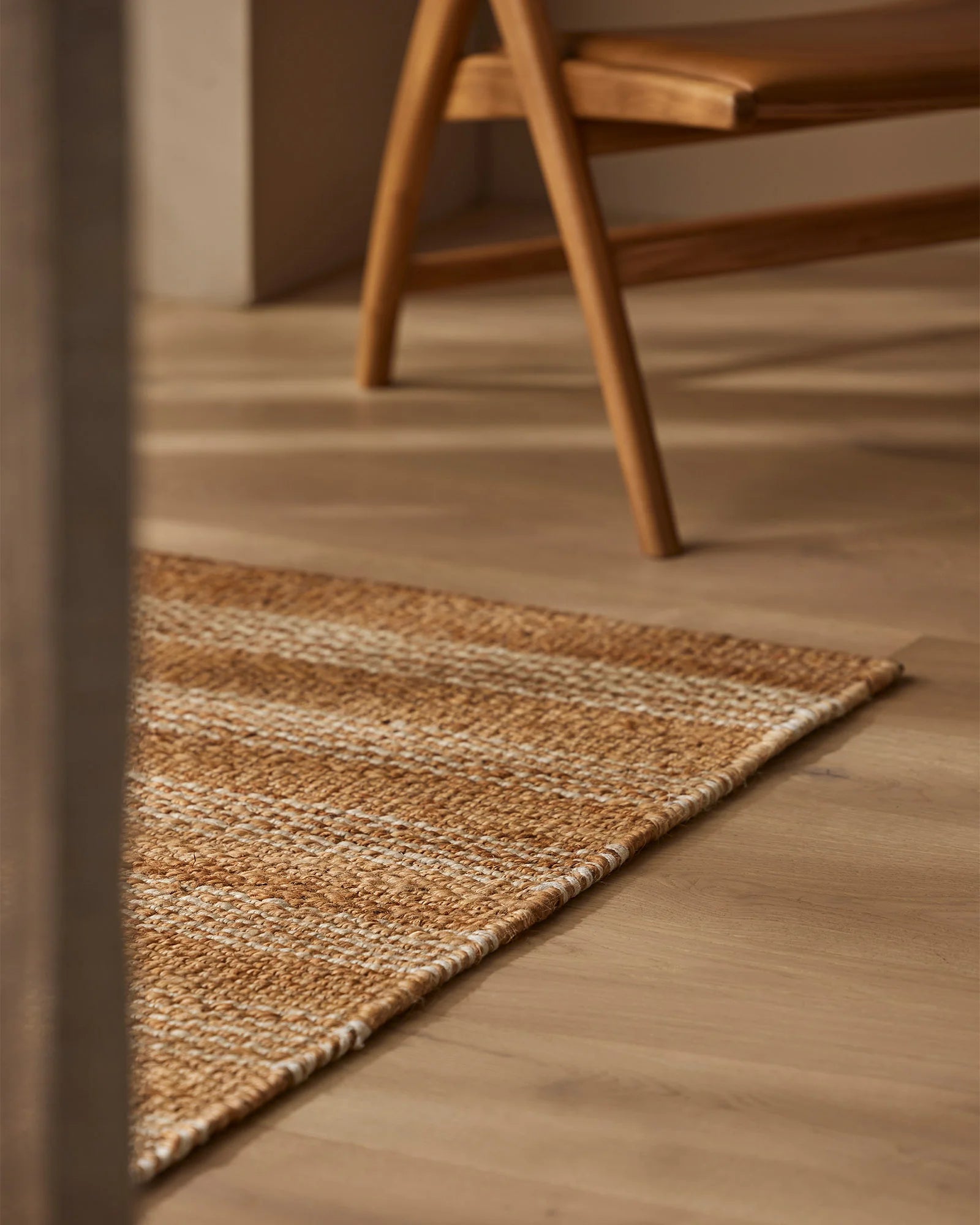 Natural jute doormat in minimalist entryway with timber flooring and mid-century wooden furniture, warm neutral palette