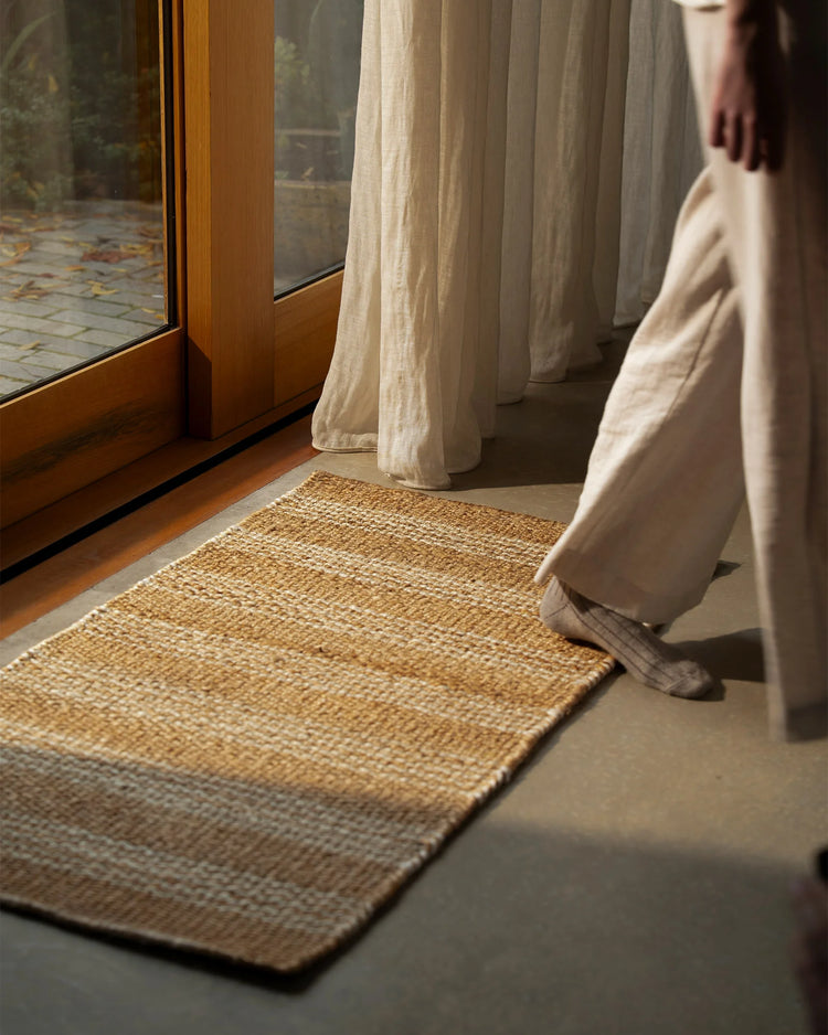 Natural linen curtains frame a warm timber window with jute doormat in minimalist entryway, neutral earthy palette with layered textures