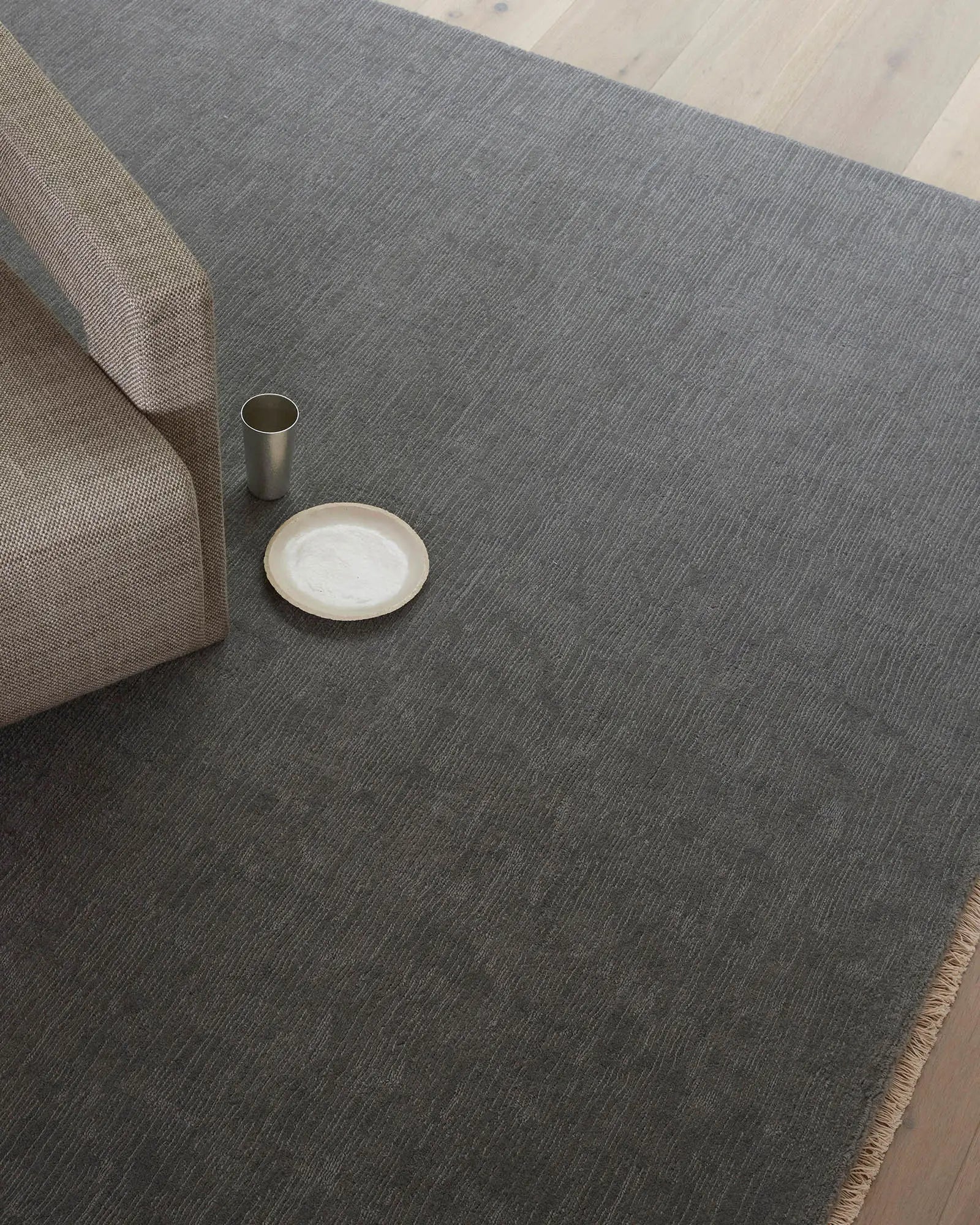 Charcoal wool rug with natural texture anchors minimalist styling, paired with neutral upholstered seating and ceramic accents on light timber floor