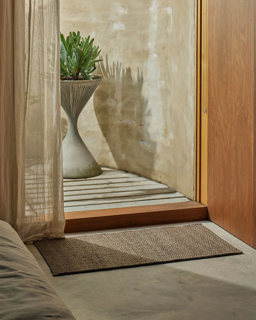 Neutral entryway with natural linen curtains, jute door mat, and whitewashed walls; succulent plant in ceramic pot adds organic texture to minimal, earthy aesthetic