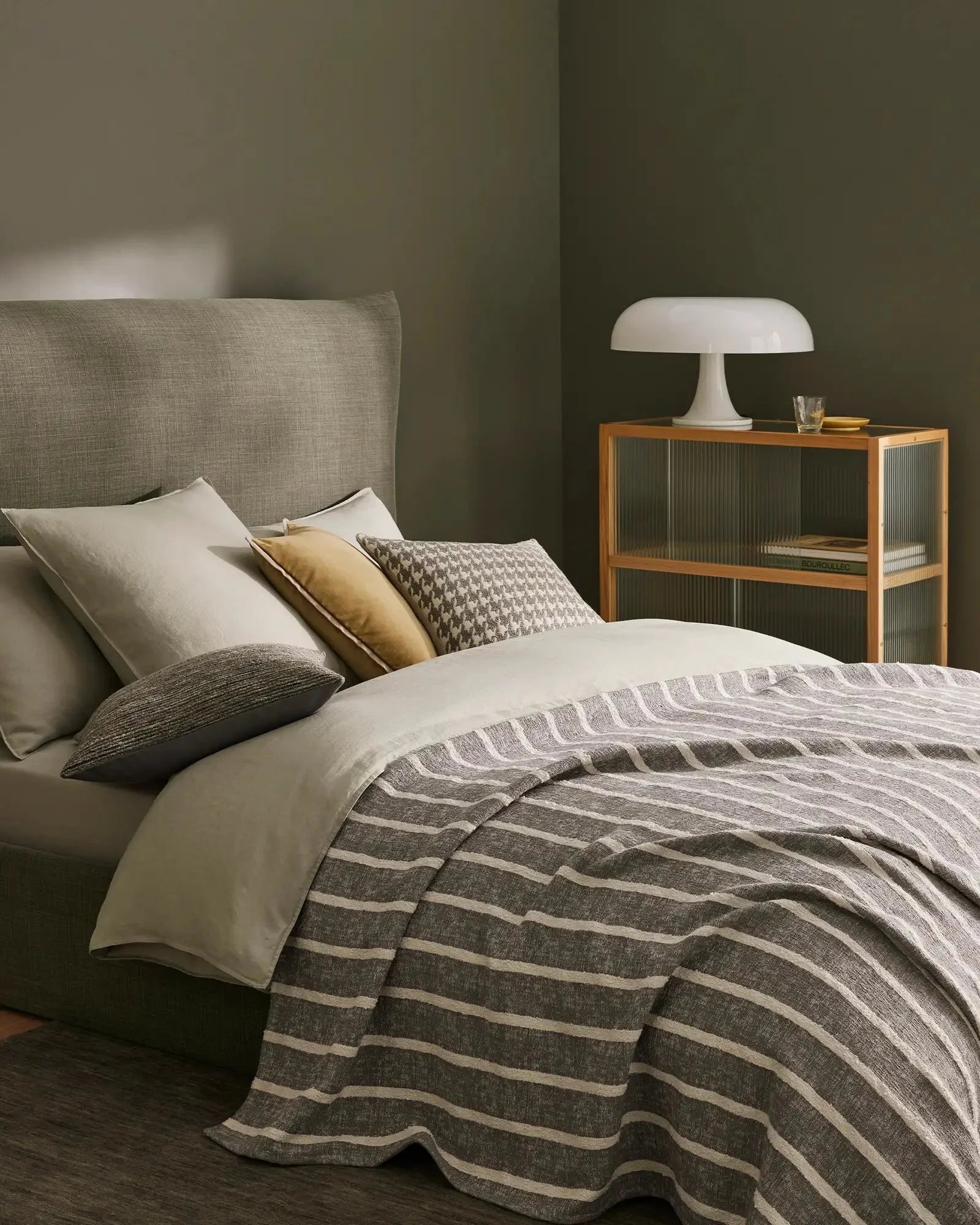 Sage green bedroom with Piazza throw in striped linen, layered with cream and gold cushions, textured Giovanni cushion, and neutral bedding for contemporary minimalist style