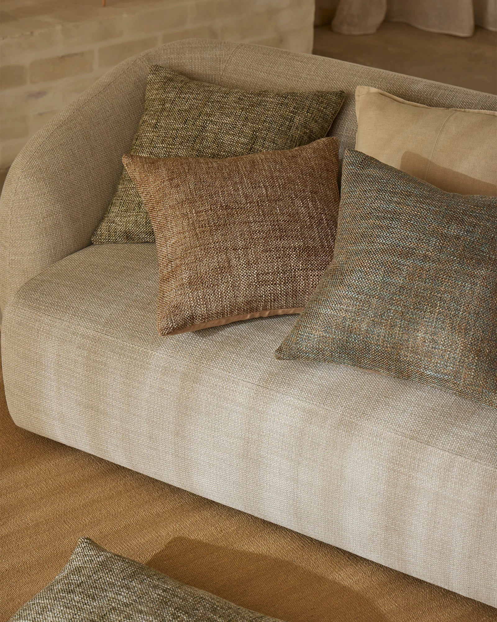 Neutral living room with cream curved armchair styled with layered sage green, olive, and caramel textured cushions in organic linen blend fabrics
