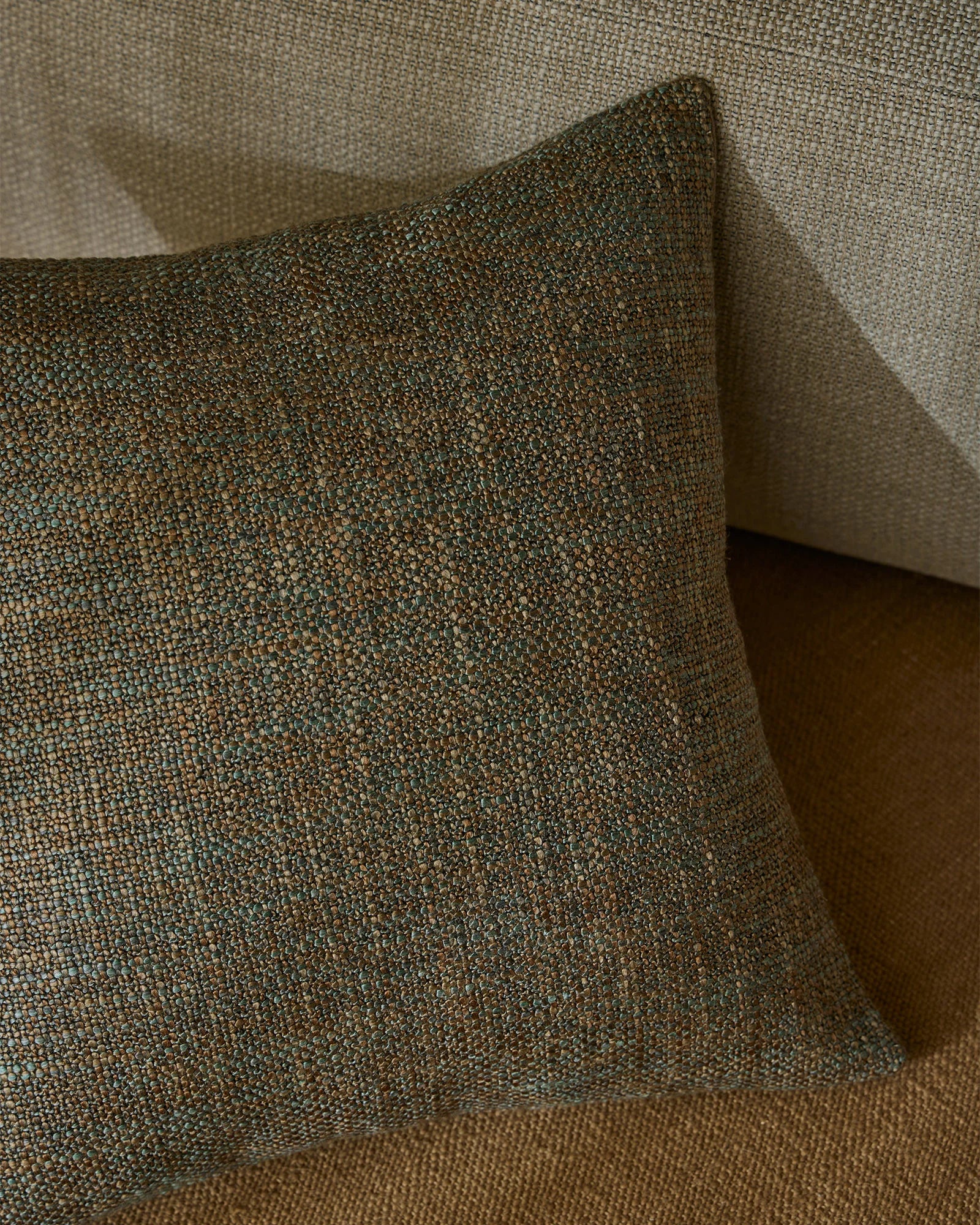 Sage green textured cushion with woven jacquard detail on neutral linen sofa, capturing natural light and tactile depth