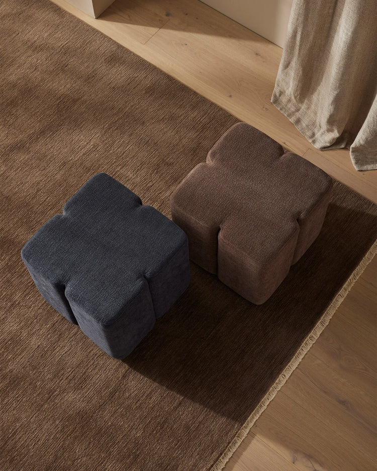 Neutral and navy linen-blend ottomans arranged on a textured area rug beside pale wood flooring, styled with draped natural linen in a minimalist living space