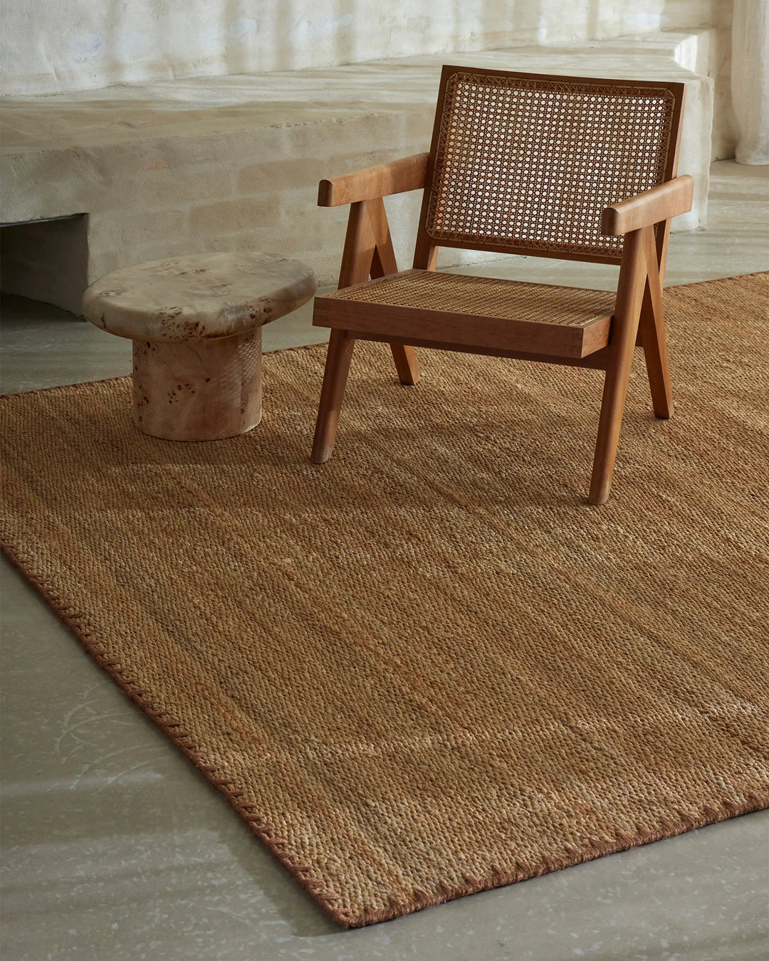 Mid-century modern lounge setting with Monroe rug in warm biscuit tone, warm wood chair with rattan detailing, and natural light filtering through sheer curtains