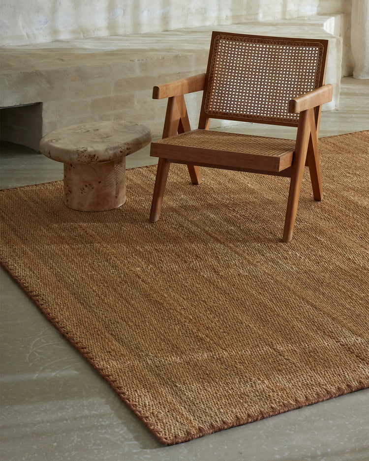 Mid-century modern lounge setting with Monroe rug in warm biscuit tone, warm wood chair with rattan detailing, and natural light filtering through sheer curtains