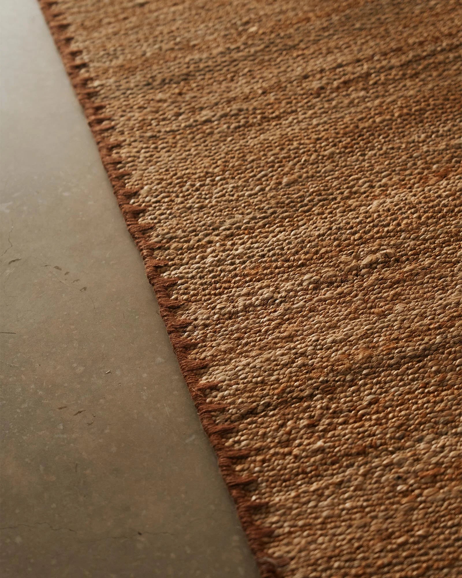 Close-up of neutral biscuit textured rug on polished concrete floor, showcasing natural woven detail and warm earthy tones in modern minimalist interior styling