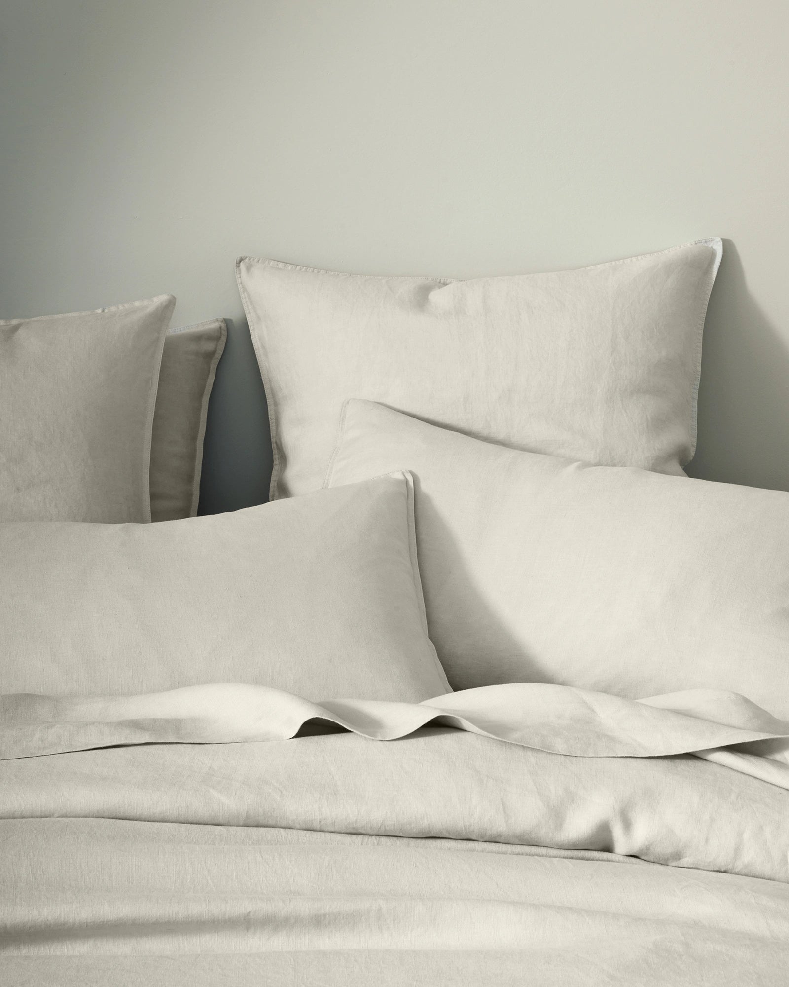 Neutral linen bedding styled flat lay with Ravello quilt cover, flat sheet and pillowcases in bone, showcasing soft European linen texture and relaxed, undone aesthetic
