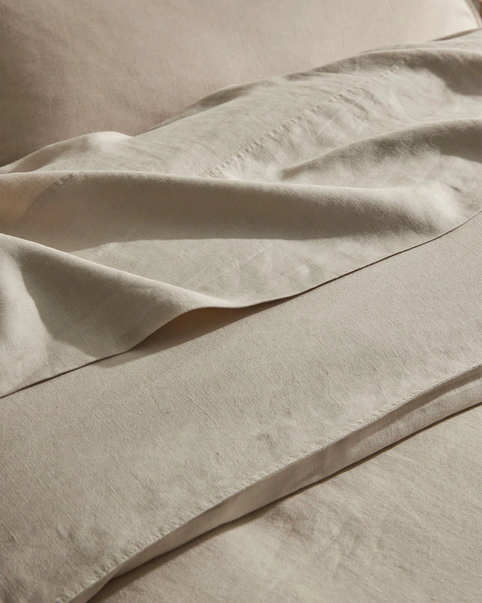 Close-up of layered natural linen bedding in cream, showing soft folds and texture of European linen sheets with tactile, relaxed styling