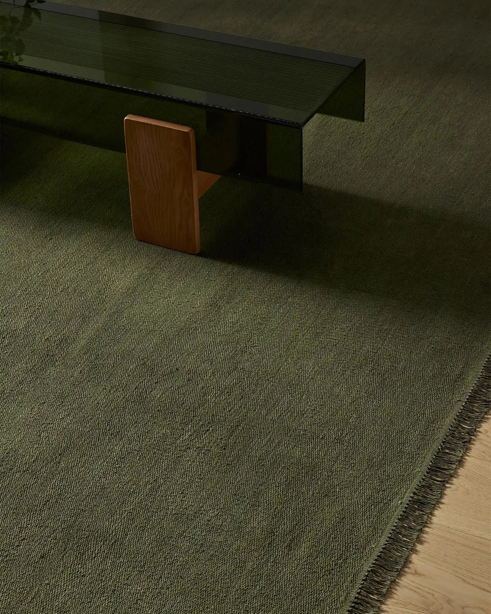 Sage green linen rug in modern minimalist interior with wooden chair and black desk, showcasing textured weave and fringed edge detailing.