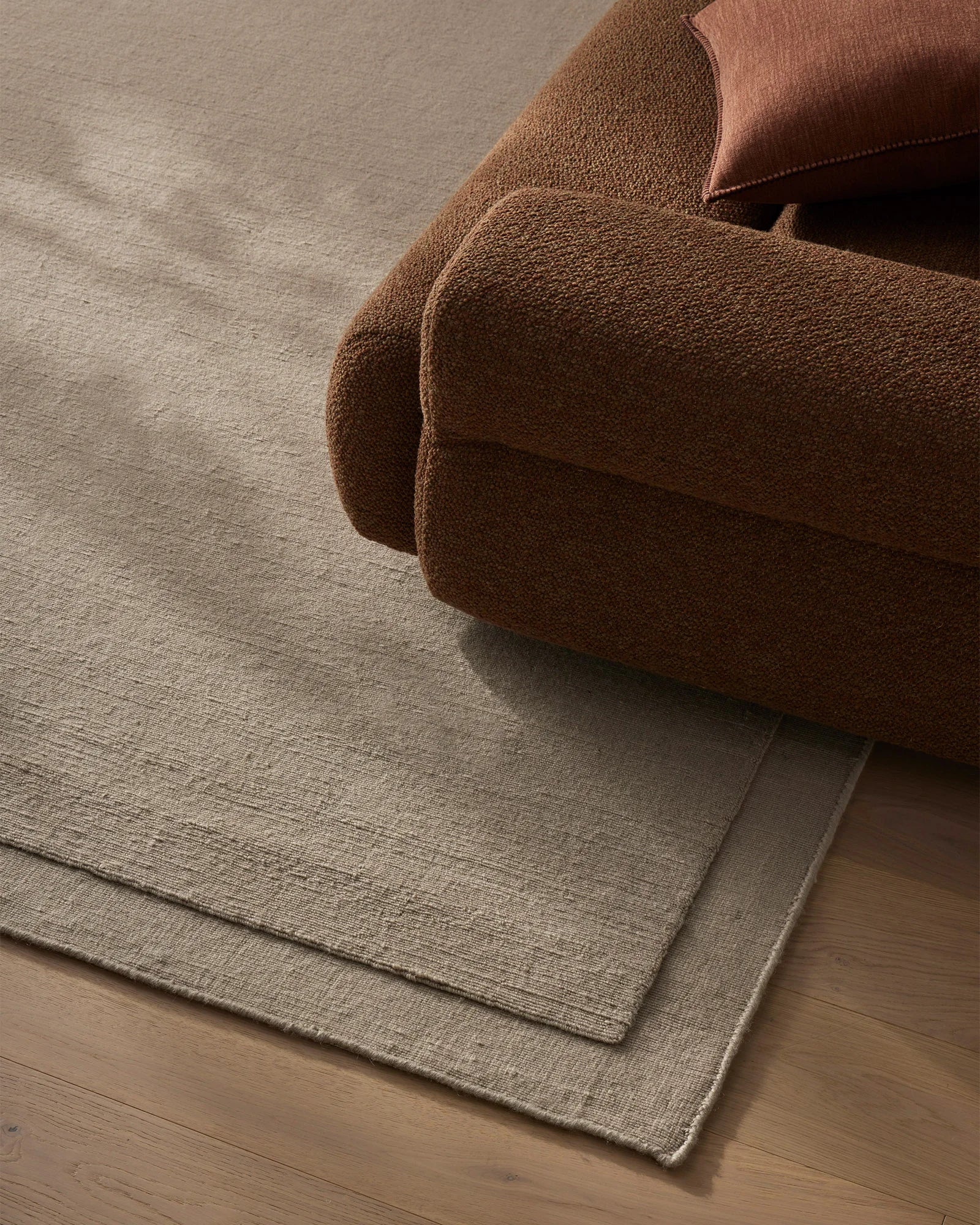 Warm terracotta throw and blush cushion layered over natural wool rug in neutral grey, showcasing textured weave and warm earth-tone palette for understated living room styling