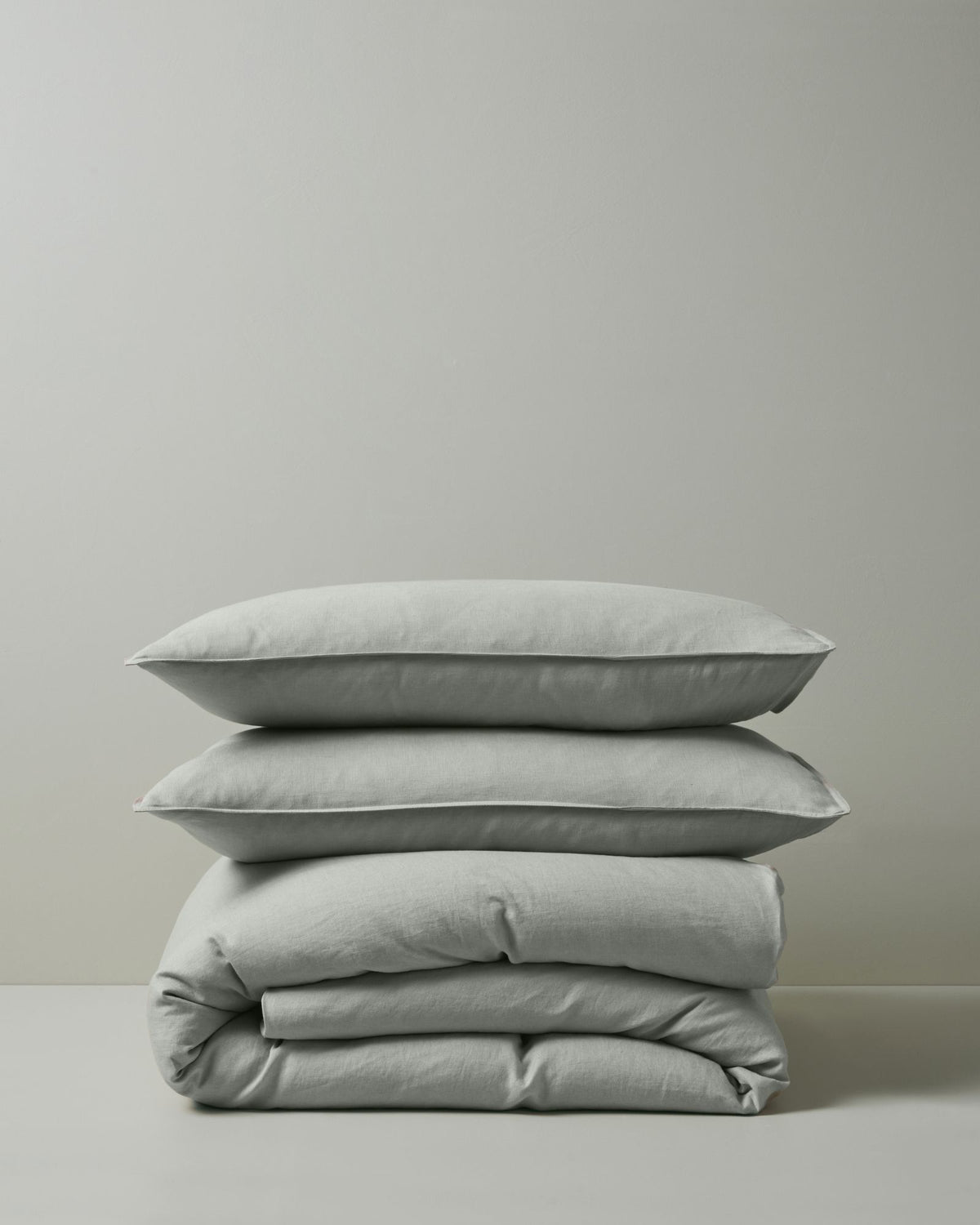 Stacked linen bedding in soft sage tones: Ravello Quilt Cover and Ravello Pillowcase set layered together, showcasing natural texture and neutral minimalist aesthetic
