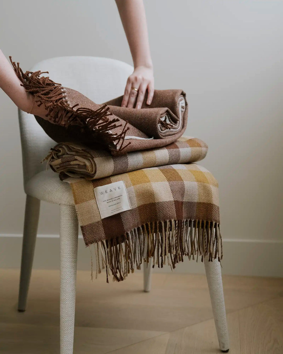 Caldwell Autumn wool throw in taupe, cocoa and ochre plaid with fringe border, draped and folded on white chair by Weave Home