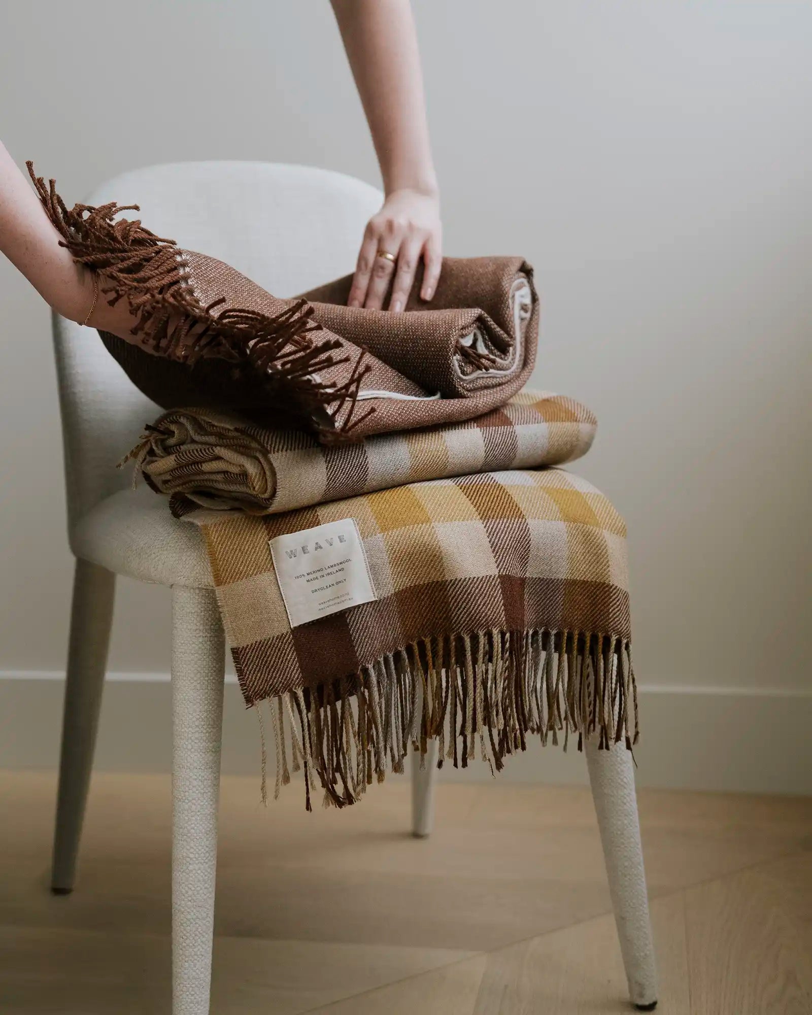 Caldwell Autumn wool throw in taupe, cocoa and ochre plaid with fringe border, draped and folded on white chair by Weave Home