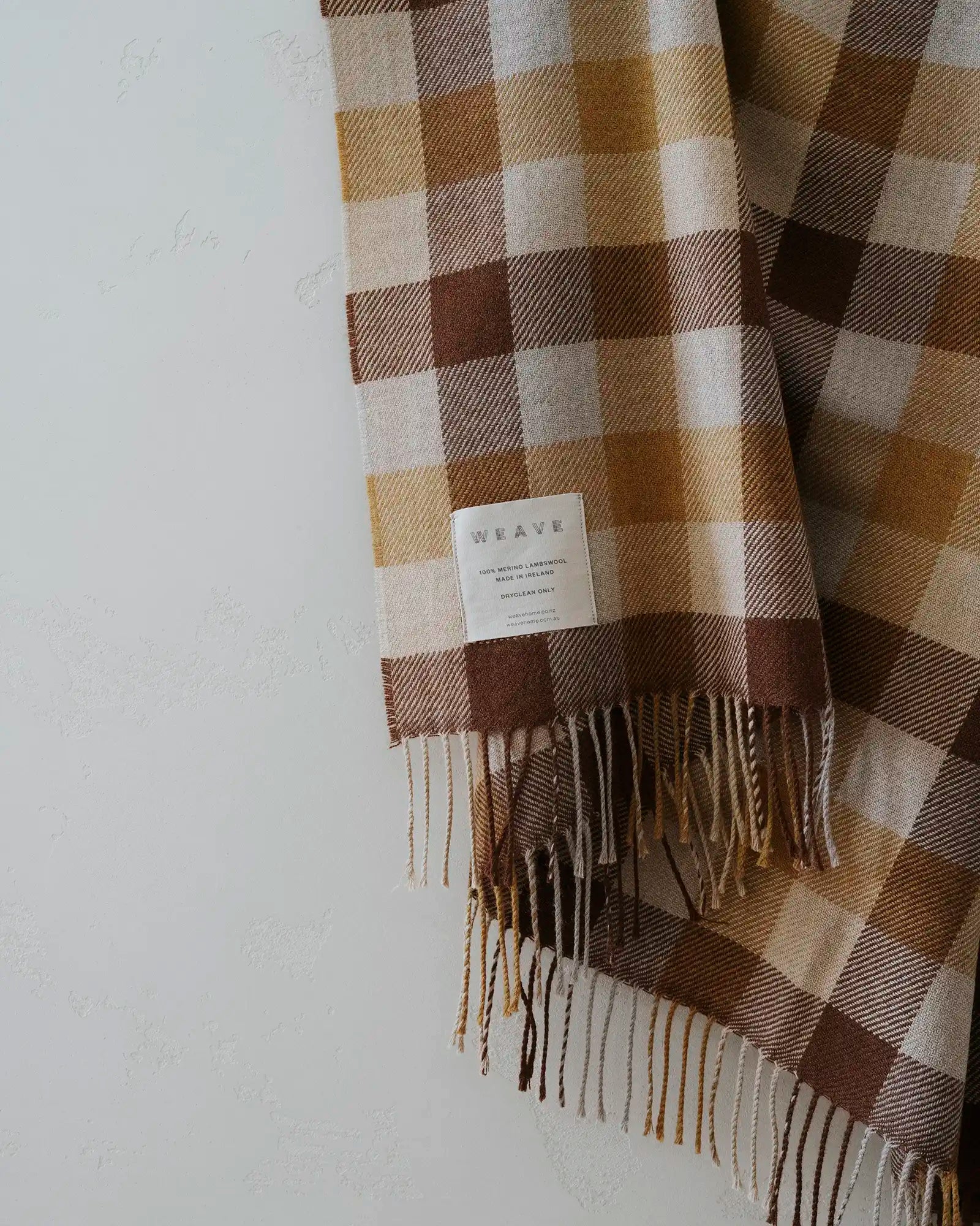 Caldwell Autumn wool throw in taupe, cocoa and ochre plaid with fringe trim, draped on light background by Weave Home