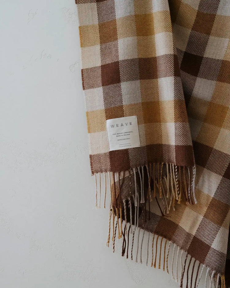Caldwell Autumn wool throw in taupe, cocoa and ochre plaid with fringe trim, draped on light background by Weave Home