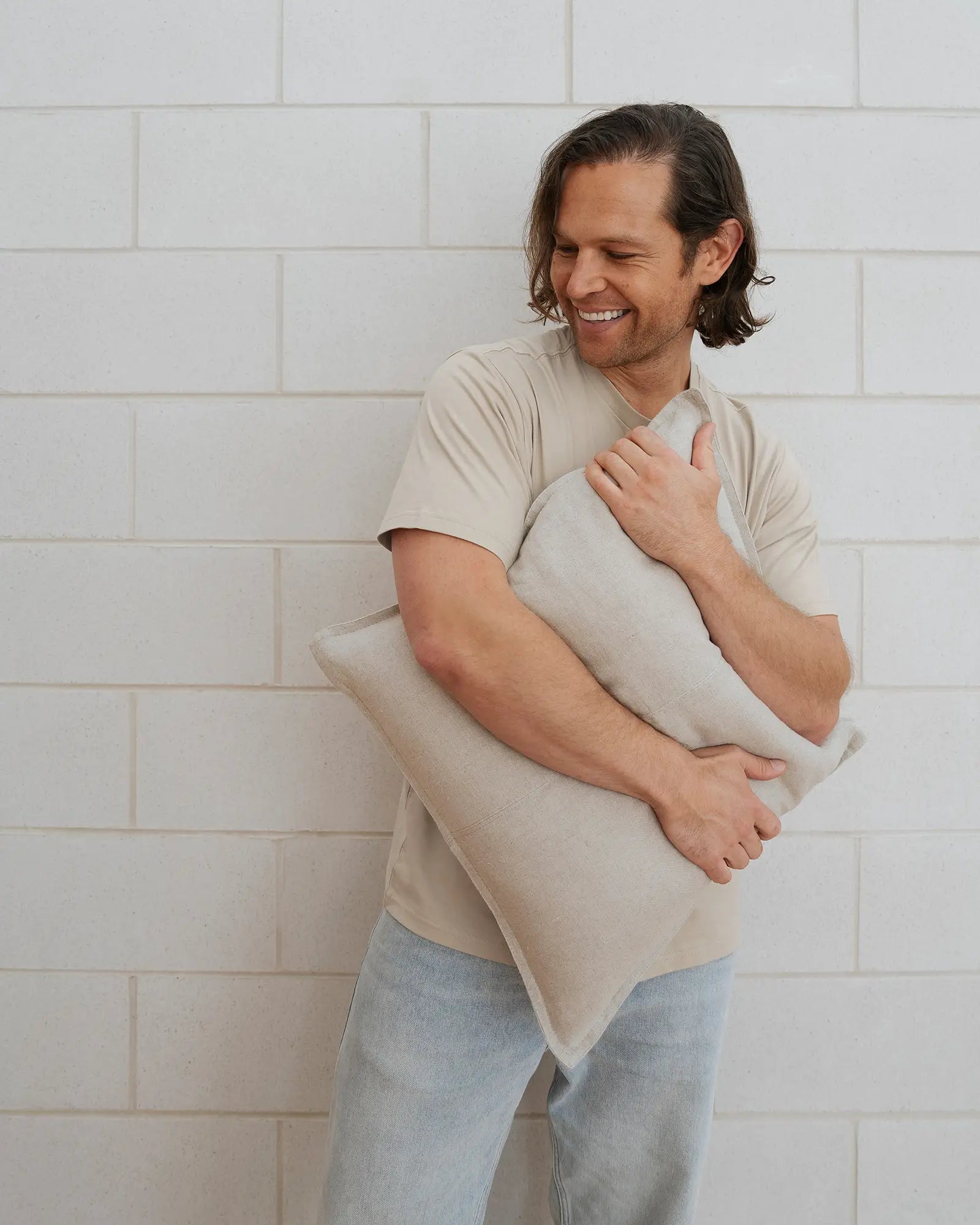 Como Linen cushion in off-white European linen, 50x50cm, held by man against white brick wall by Weave Home