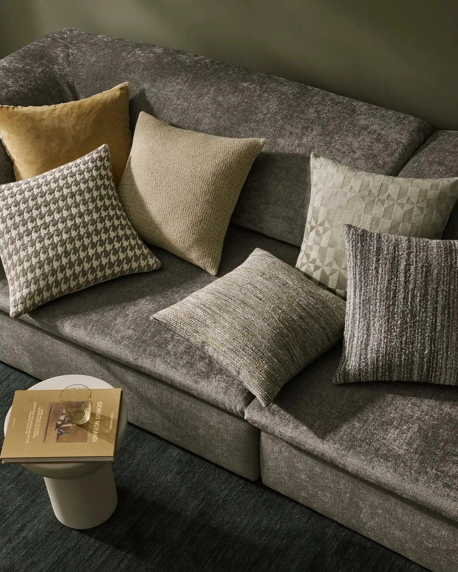 Neutral living room with grey upholstered sofa styled with textured cushions in cream, gold and sage tones featuring Giovanni and Marina ranges showcasing layered textile patterns and weaves