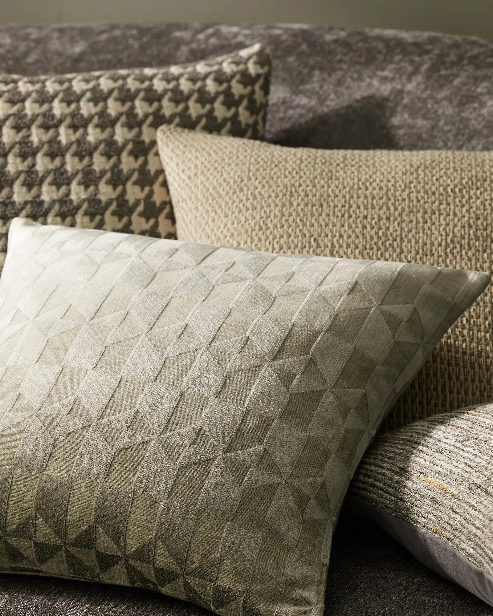 Neutral layered cushions in sage and cream linen blends styled on a sofa, featuring quilted geometric textures and woven patterns in warm greige tones