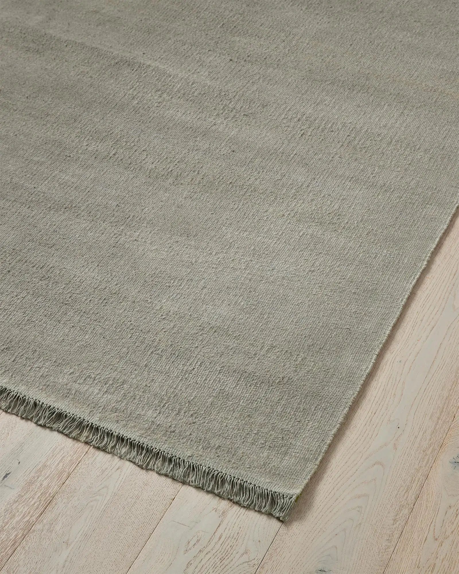 Emilio Flint linen rug corner detail, showing soft grey-blue flat-weave with fringe edge by Weave Home