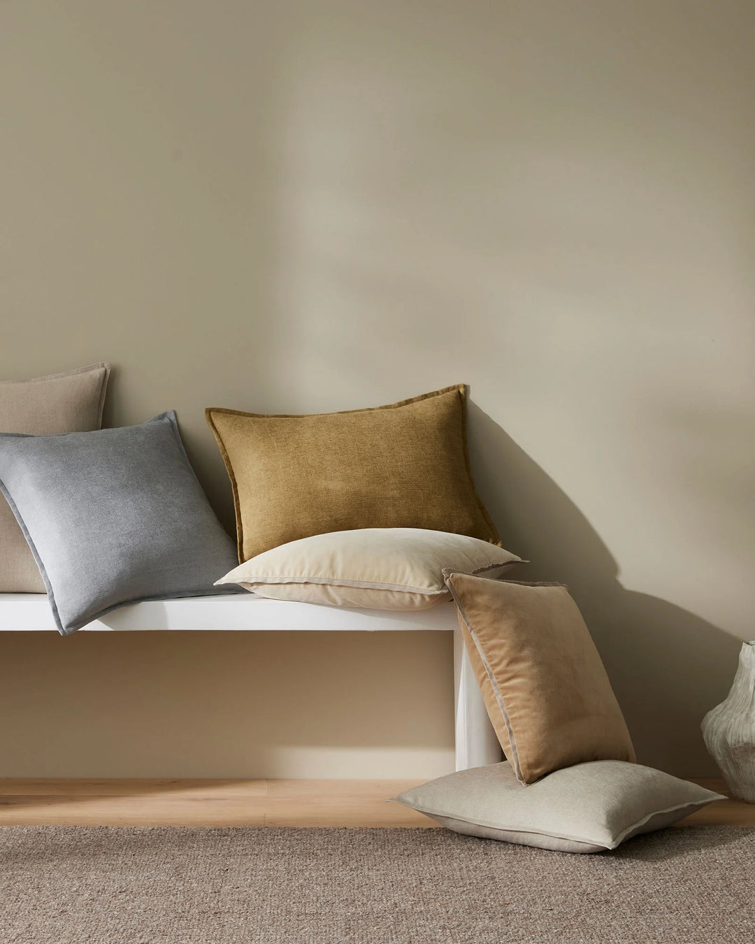 Neutral minimalist styling with Francesca copper cushion and coordinating sage, stone, and cream pillows arranged on white platform bed with natural linen textures and soft shadows