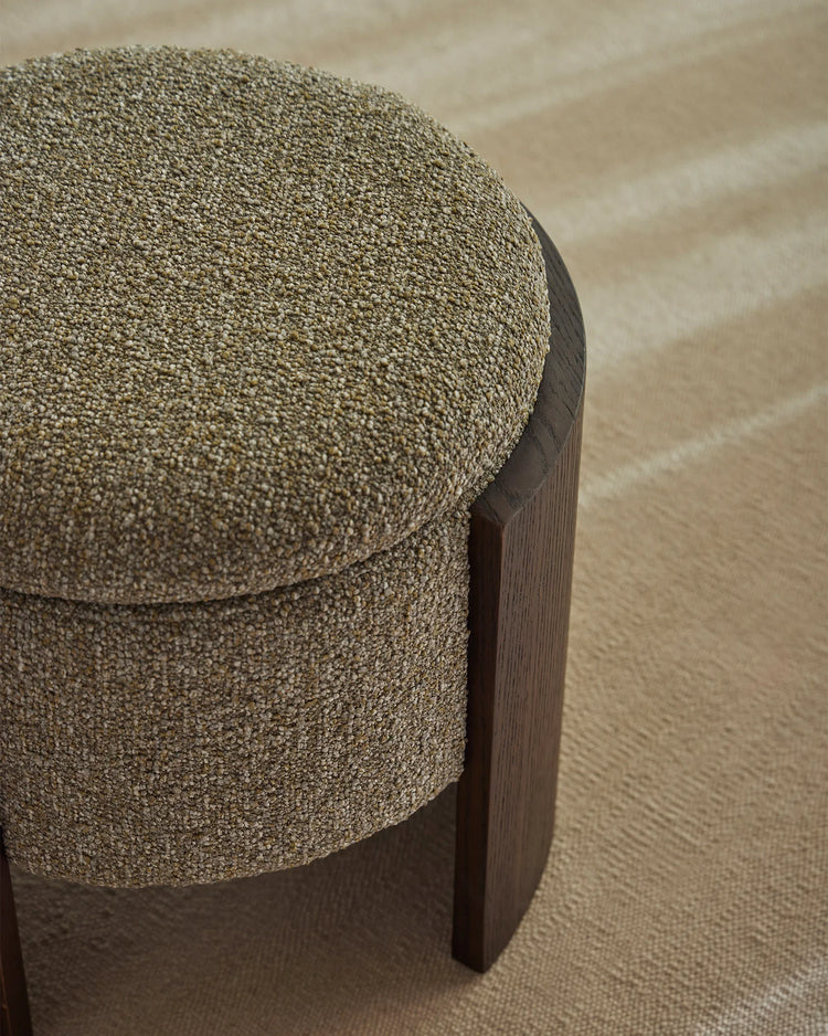 Sage green boucle ottoman with dark timber base on neutral textured flooring, modern minimalist home décor styling with warm earthy tones