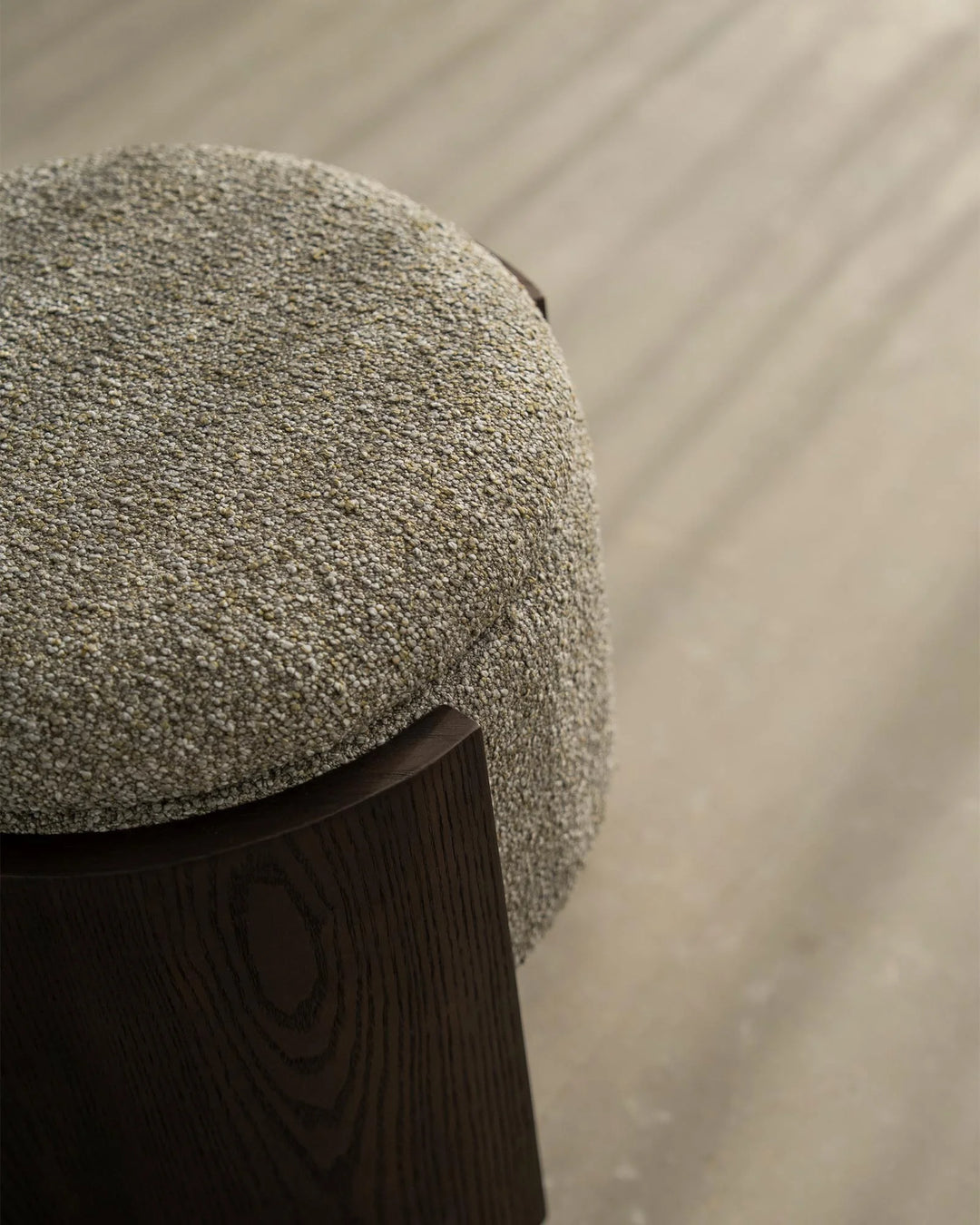 Sage green boucle ottoman with dark timber base on neutral linen background, showcasing textured upholstery and minimalist Scandinavian styling