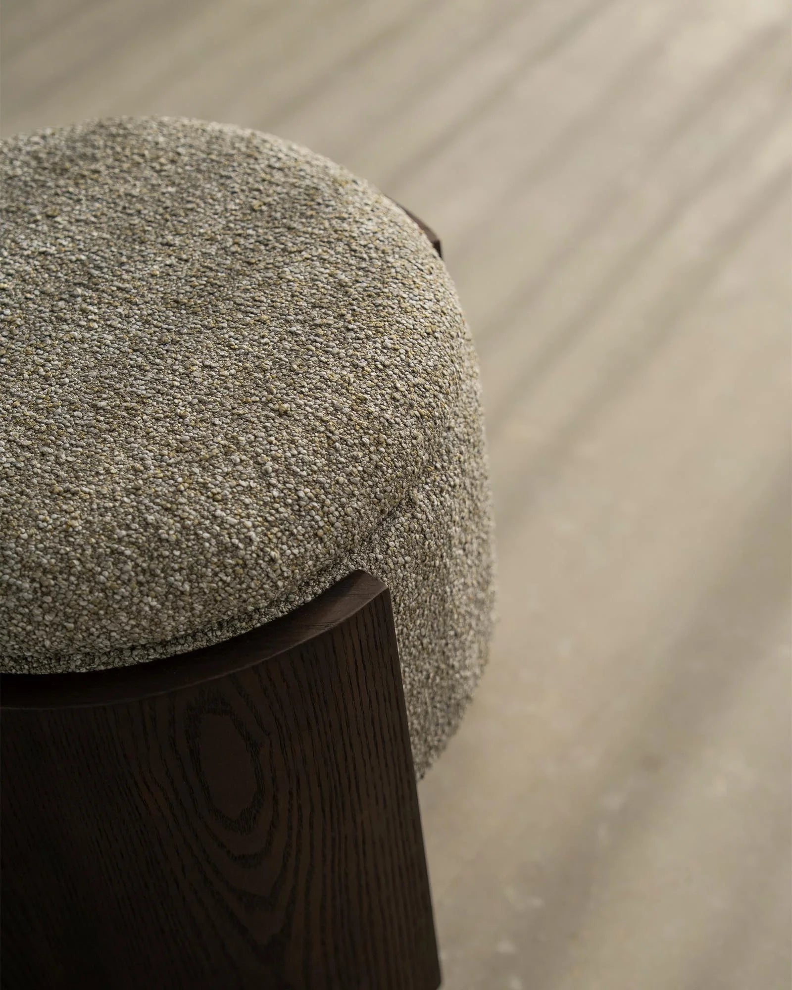 Sage green boucle ottoman with dark timber base on neutral linen background, showcasing textured upholstery and minimalist Scandinavian styling
