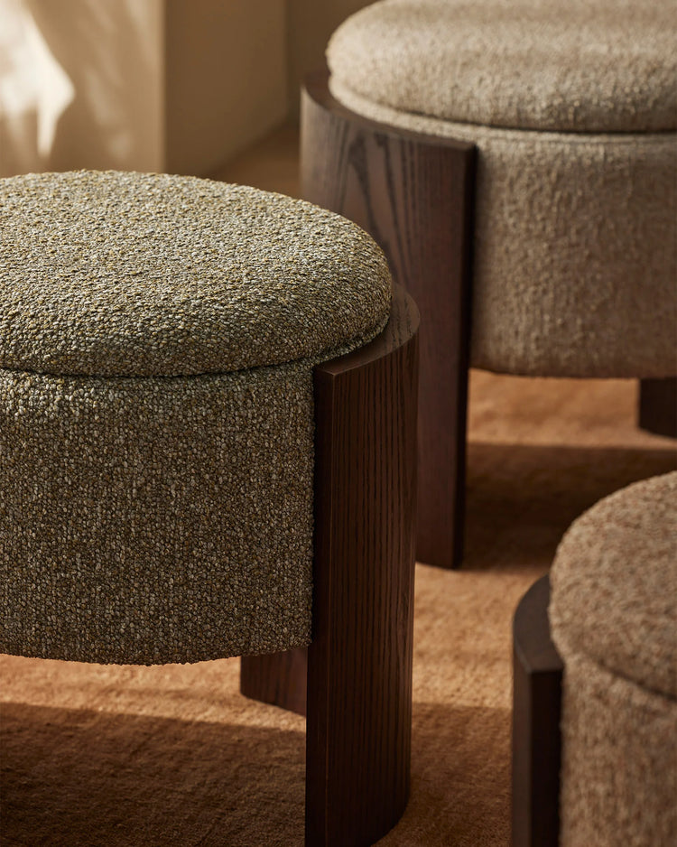 Warm-toned styling featuring sage-green upholstered ottomans with dark wood legs, layered on natural jute rugs in a soft, neutral interior scheme