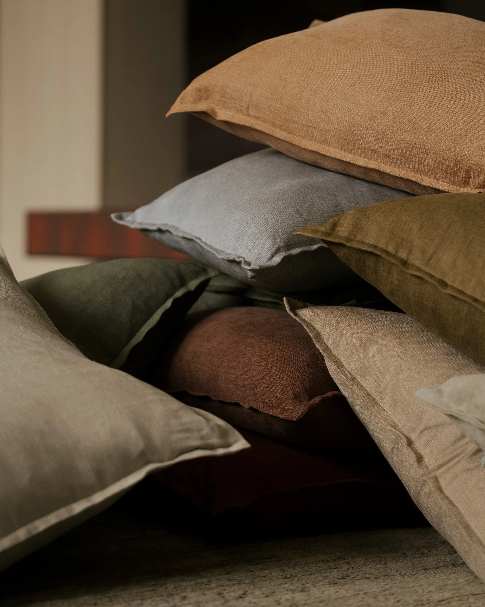 Layered Fiore cushions in earth tones and muted greens showcase linen viscose blend textures, creating a warm, minimalist composition with natural colour palette