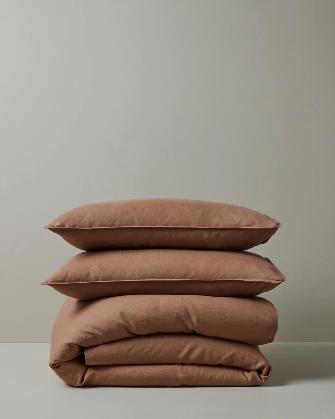 Stacked Ravello Quilt Cover and Pillowcase Set in biscuit, showcasing warm terracotta and neutral tones with soft linen texture and minimalist styling