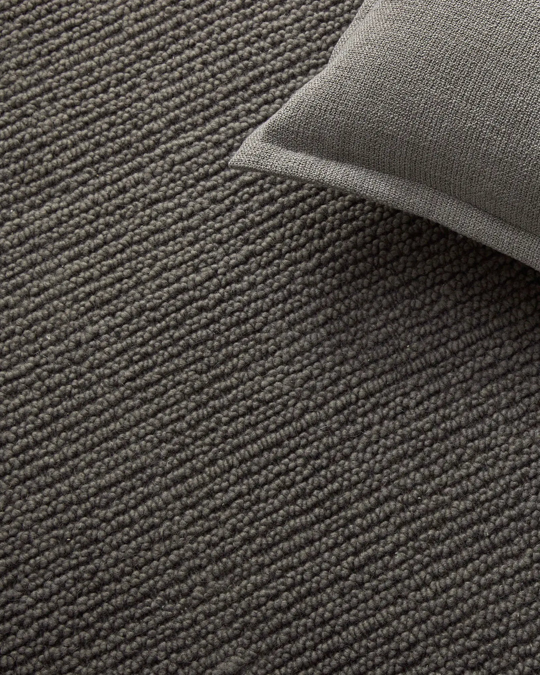 Layered neutral wool rugs in charcoal and fog grey tones, showcasing textured woven surfaces and subtle tonal variations in a minimalist interior styling